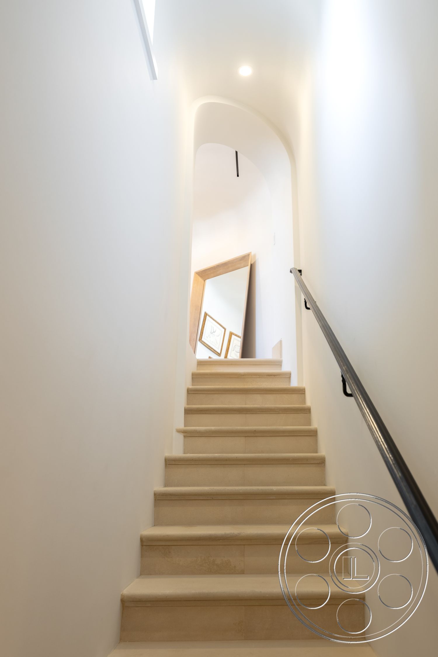 Spanish 168 - neutral color palette, open concept design, minimalist architectural style, metal stair railing, natural light from upper windows, interior limestone staircase, smooth white plaster walls, arched stairway design, built-in wall artwork frames, soft beige stair treads