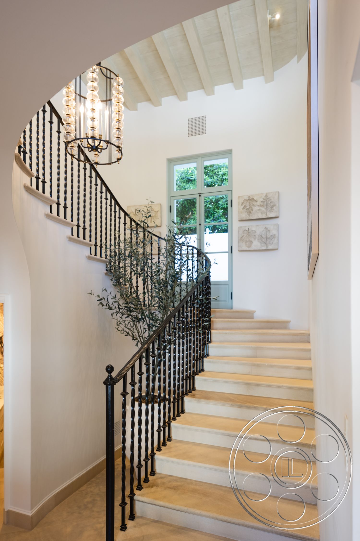 Spanish 168 - neutral color palette, floor-to-ceiling windows, decorative wall art, soft natural lighting, textured plaster walls, black wrought iron railings, exposed wood ceiling beams, open staircase design, large arched doorway, interior spiral staircase, light-colored stone steps, modern chandelier fixture, verdant indoor plant, bright entryway aesthetic