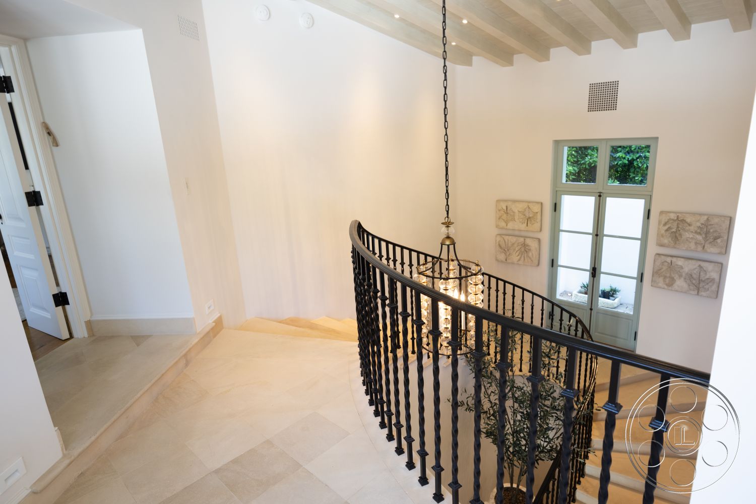 Spanish 168 - neutral color palette, natural light, textured wall art, open space layout, arched doorways, black wrought iron railing, exposed wood ceiling beams, white painted walls, glass panel doors, marble floor tiles, chandelier lighting fixture, interior curved staircase, multi-level foyer