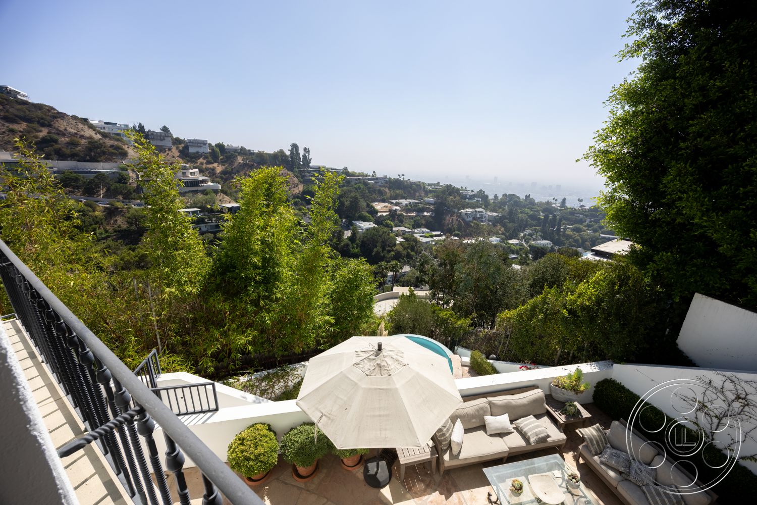 Spanish 168 - exterior view, sloping terrain, city skyline view, contemporary outdoor space, rectangular pool, minimalist garden design, concrete pool border, natural stone patio flooring, lush greenery landscaping, open-air relaxation area, potted plants decor, suburban hillside setting, wood deck patio furniture, glass outdoor table, tiled outdoor seating area, horizontal wood railings, modern storm umbrella, sunny outdoor living area