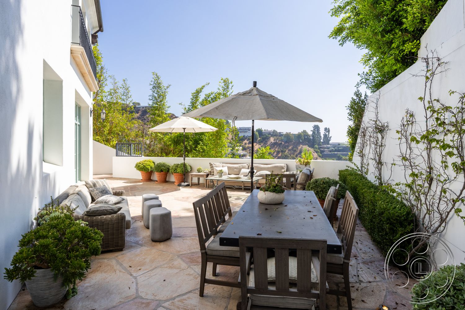 Spanish 168 - potted plants, wood dining table, planter boxes, contemporary outdoor decor, modern outdoor seating, natural stone patio flooring, lush greenery landscaping, sunny hillside location, exterior patio space, textured white plaster walls, concrete garden stools, canvas umbrella, climbing vines on walls, horizontal slat privacy screen