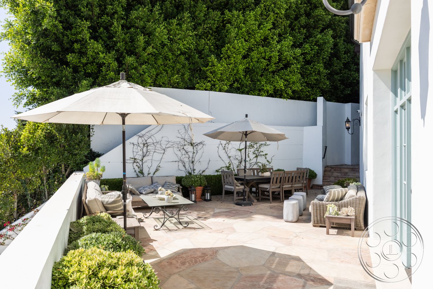 Spanish 168 - natural light, exterior, lush greenery backdrop, minimalist outdoor decor, concrete retaining wall, rustic outdoor seating area, sunny hillside location, flagstone patio flooring, outdoor dining area with wooden table, beige canvas patio umbrellas, green succulent garden border, textured white stucco wall, stone accent planter pots, weathered wooden lounge furniture, modern outdoor coffee table, garden patio setting, urban balcony retreat