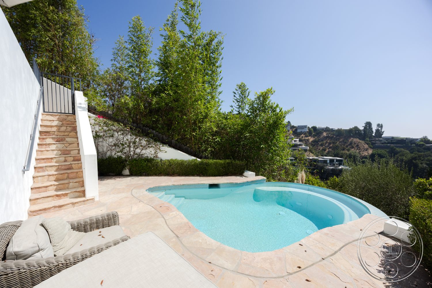 Spanish 168 - exterior, white stucco walls, outdoor lounge area, city skyline view, stone pool deck, curved pool edge, oval swimming pool, contemporary architectural style, metal stair railings, natural stone patio flooring, concrete patio border, landscaped garden with bamboo, textured stone steps