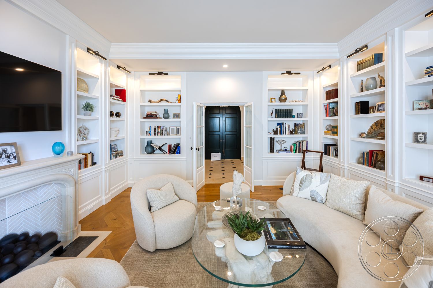 Spanish 168 - neutral color palette interior, dark wood paneling interior, exposed wood ceiling beams interior, white painted walls interior, hardwood living room floors interior, minimalist decorative accents interior, textured plaster walls interior, beige upholstered circular sofa interior, glass coffee table interior, bookshelves with decorative items interior, natural light through large windows interior, luxury contemporary design interior, modern fireplace surround interior, open layout floor plan interior, decorative plant feature interior, trimmed crown molding details interior, built-in storage shelves interior, black double doors entry interior, area rug for comfort interior