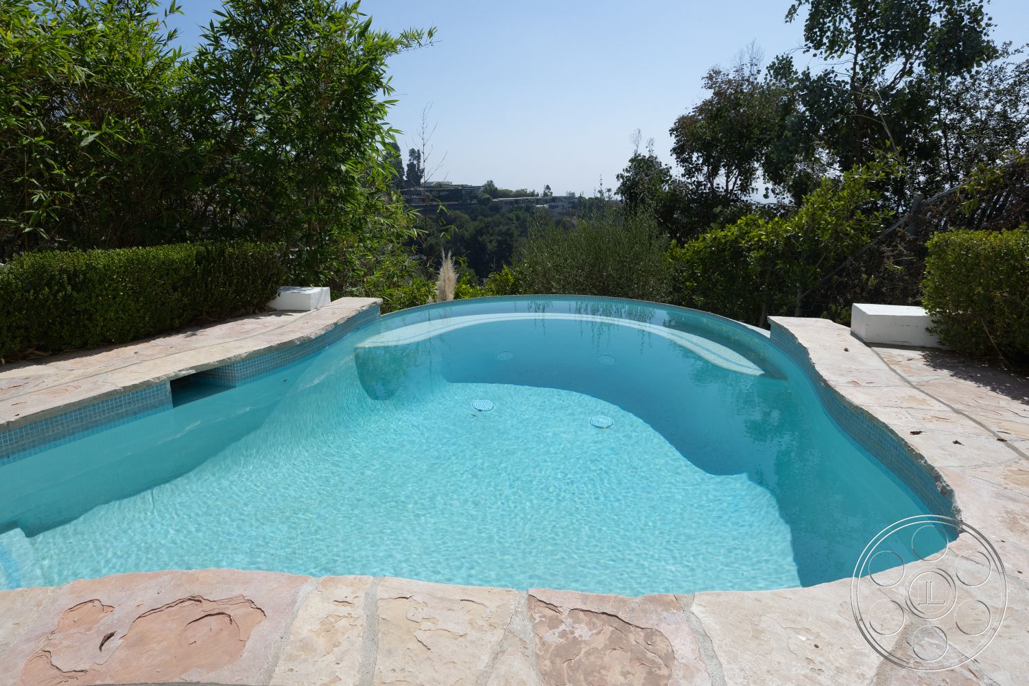 Spanish 168 - surrounding greenery, infinity pool, landscaped garden setting, bamboo privacy screening, sunny outdoor environment, natural stone pool deck, irregular-shaped pool, outdoor hillside view, light blue pool water, smooth stone coping