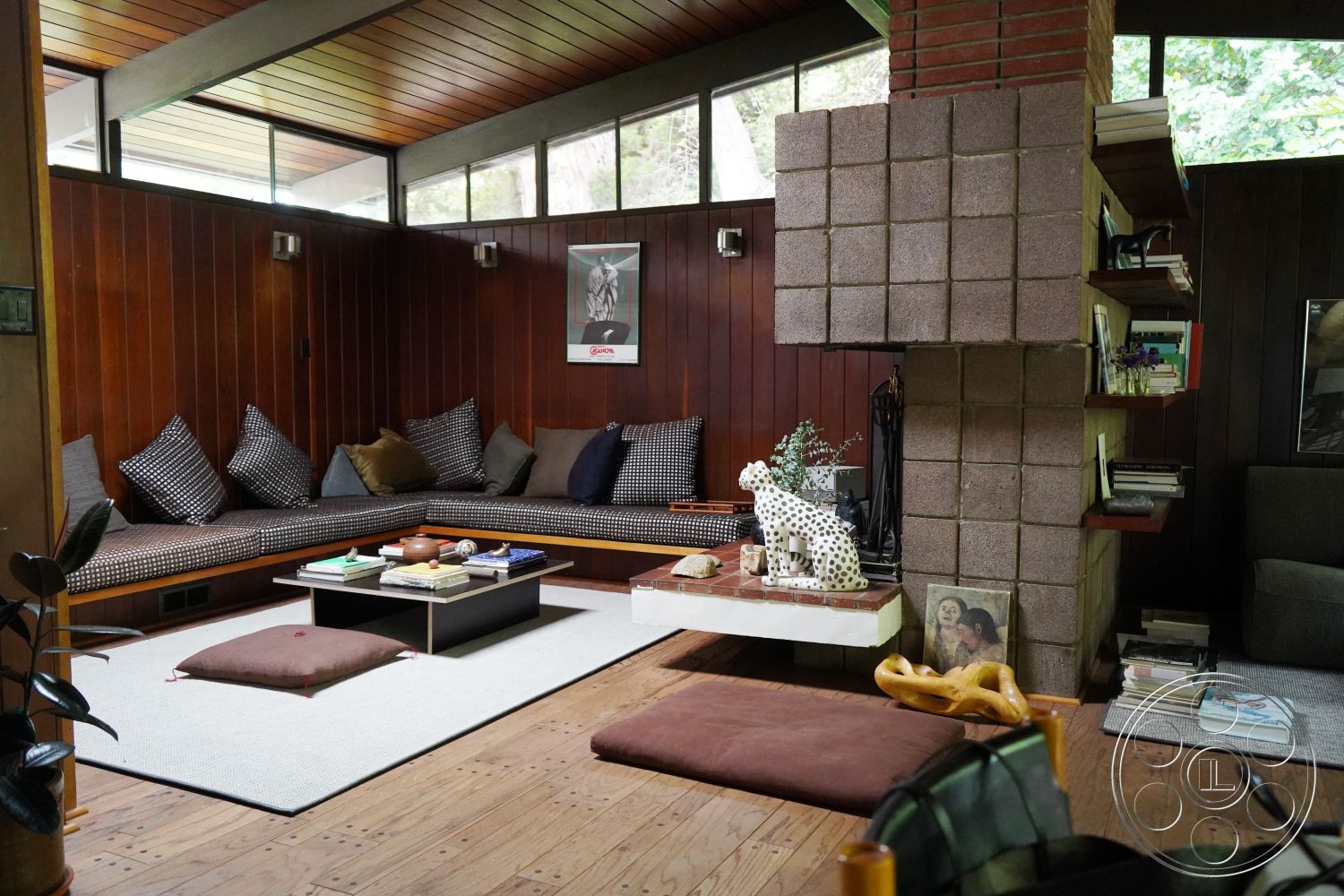 MCM 25 - floor-to-ceiling windows, natural light from large windows, cozy reading nook, contemporary coffee table, built-in bookshelves, mid-century modern architectural style, neutral color palette interior, open concept living area, polished hardwood flooring, textured plaster accent wall, square room layout, exposed wood paneling interior, rectangle floor cushions, tile fireplace surround, glass block fireplace wall, low-profile seating arrangement, earthy tones in decor, urban forest setting, dynamic spatial flow interior, functional modern design