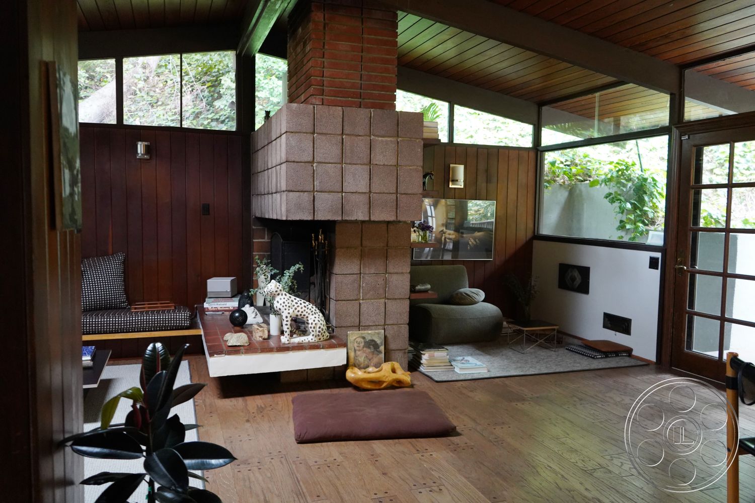 MCM 25 - natural wood flooring, earthy color palette, cozy reading nook, wooden French doors, exposed wood ceiling beams, contemporary lounge area, brick fireplace surround, open floor plan interior, glass window walls, wood paneling walls, rustic modern style, textured plaster wall details, rectangular living room layout, modern furniture accents, surrounding green landscape views