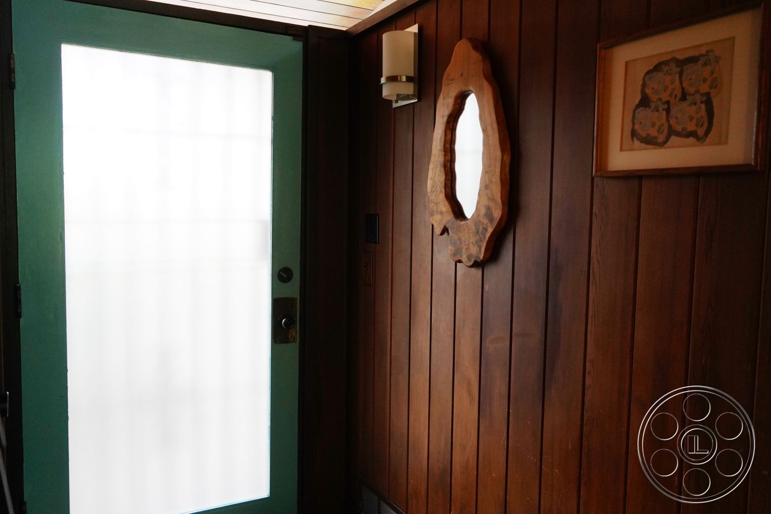 MCM 25 - textured plaster ceiling, interior wood paneling, exposed wood accent wall, glazed entry door, natural wood mirror frame, ambient wall sconce lighting, earthy tone decor, functional entryway space