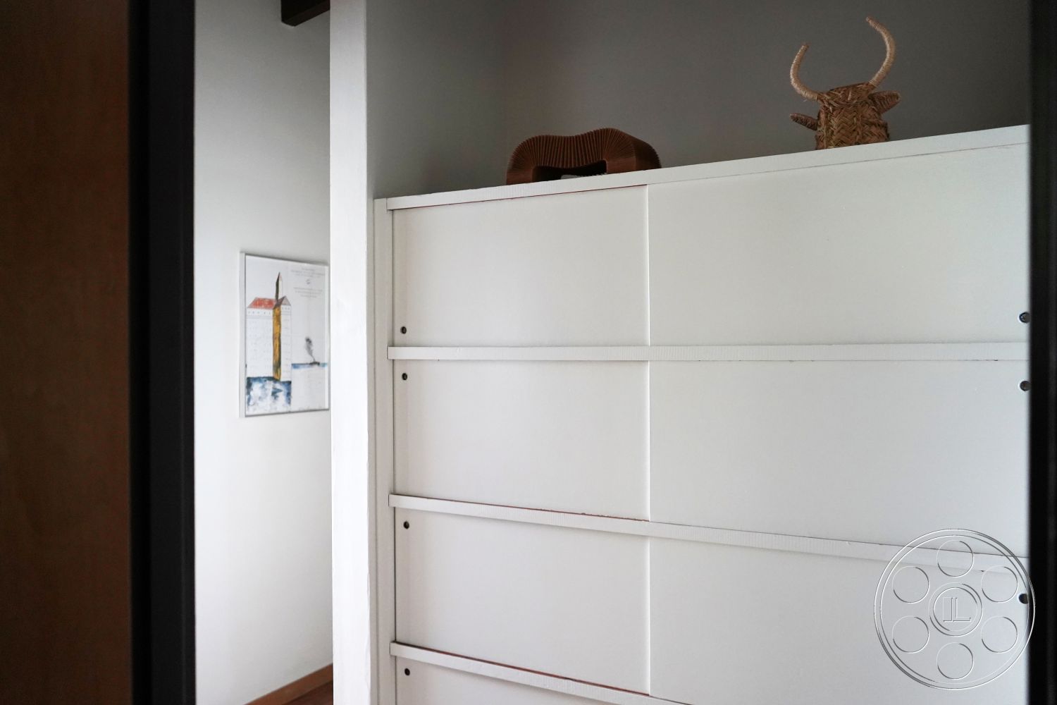 MCM 25 - hardwood flooring, dark wood door frame, white laminate cabinetry interior, neutral gray painted walls, minimalist wall art framed, simple geometric shelf design, modern aesthetic interior, understated decor elements