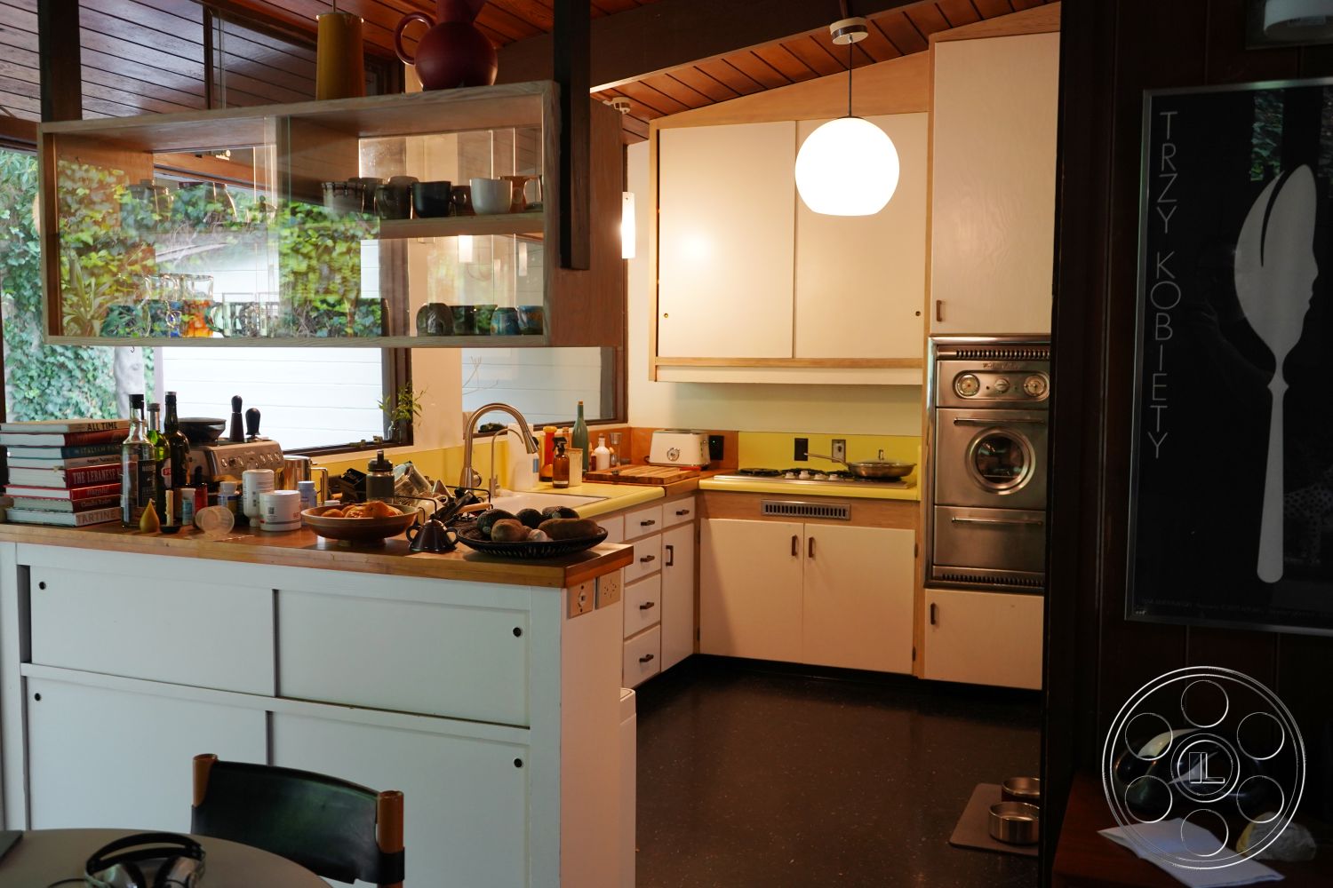 MCM 25 - stainless steel appliances, modern pendant lighting, contemporary kitchen design, exposed wood paneling, interior kitchen with wooden ceiling beams, white lacquered cabinetry with laminate accents, glass front kitchen shelving, hardwood kitchen countertops, yellow countertop detail, open shelving for dishware, kitchen island workspace, urban kitchen setting with plants, functional chef's kitchen layout, decorative kitchen accessories and cookbooks