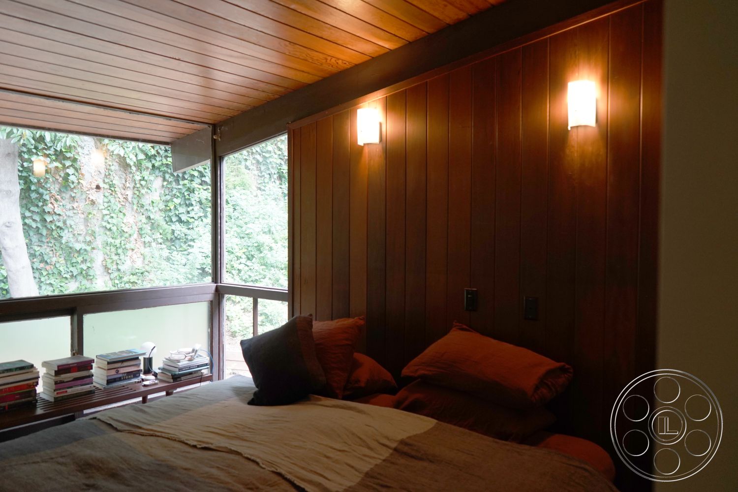 MCM 25 - modern minimalist decor, contemporary bedroom design, glass window wall, wood ceiling panels interior, wood paneling bedroom walls, built-in wood bookshelf, table lamp lighting fixtures, earthy color bedding, natural light bedroom, forest view setting