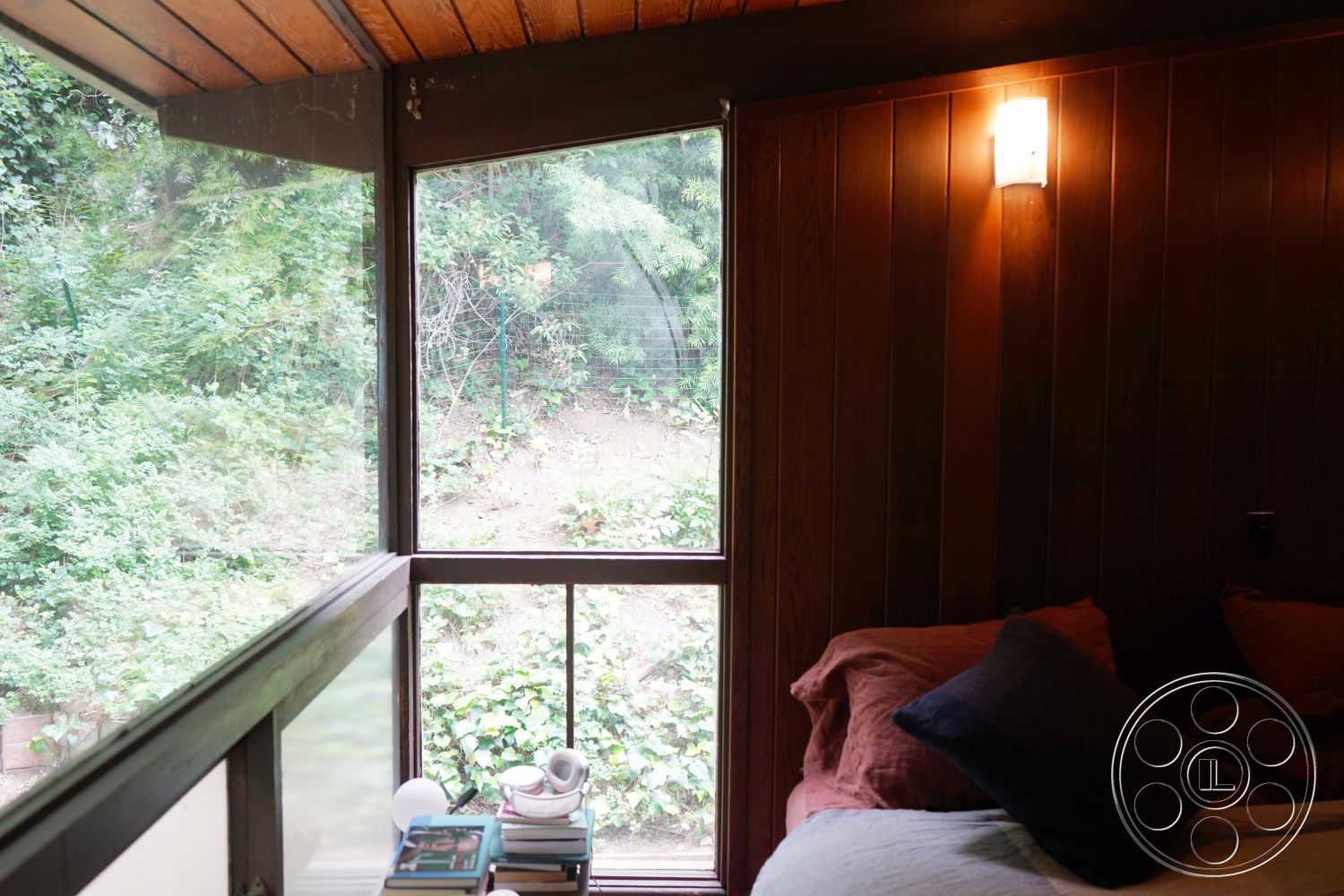 MCM 25 - exposed wood paneling interior, soft lighting fixtures interior, sloped wood ceiling with beams interior, large glass windows for natural light interior, modern minimalist bedroom atmosphere interior, organic forest view setting, wooden bedside table with books interior, plush bedding with textured pillows interior