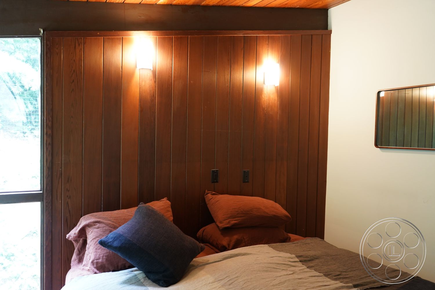 MCM 25 - interior vaulted ceiling with wooden beams, interior hardwood wall paneling, interior soft lighting fixtures, interior large windows with natural light, interior brown wall accent with lighting, interior king-size bed with brown linens, interior decorative blue pillow on bed, interior modern mirror on wall, interior cozy bedroom setting, interior muted earth tones