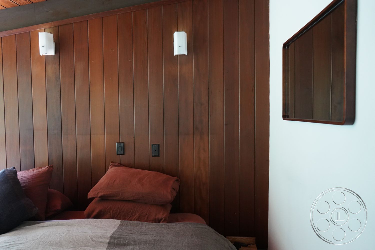MCM 25 - earthy color palette, textured plaster wall, interior bedroom setting, wood beam ceiling, farmhouse style decor, exposed wood paneling wall, velvet throw pillows, minimalist wall-mounted lighting, modern wooden mirror, soft bedding materials