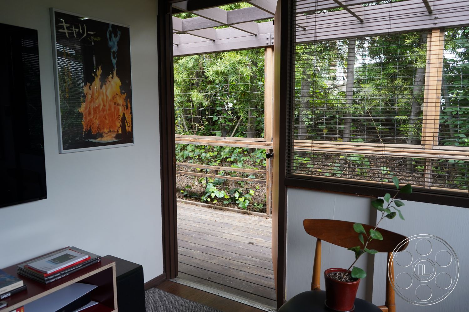 MCM 25 - warm wood tones, modern art wall decor, exposed wooden beams, glass sliding door, interior wood paneling, contemporary architectural style, exterior wooden deck, lush green landscaping view, natural light from exterior, textured white plaster walls, potted indoor plant, hardwood floor living area, open doorway design, privacy slatted wood screen