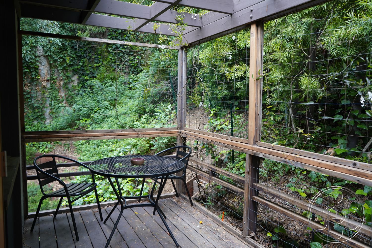 MCM 25 - natural wood materials, outdoor dining area, rustic aesthetic, surrounding landscape, metal patio furniture, wood deck flooring, exterior garden view, wood railing details, pergola roof structure, lush green foliage setting, interior patio space