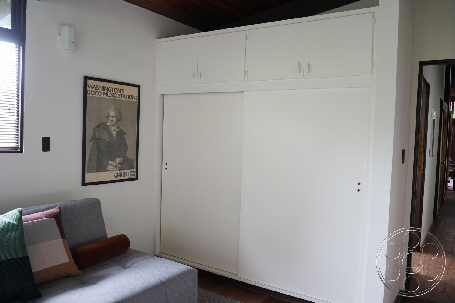 MCM 25 - neutral color palette interior, exposed wood ceiling beams interior, white painted walls interior, framed art wall decor interior, hardwood flooring living room interior, sliding closet doors white finish interior, contemporary furniture design living room interior, paneled wall storage unit interior, soft throw pillows multi-colored interior, natural light window treatment interior
