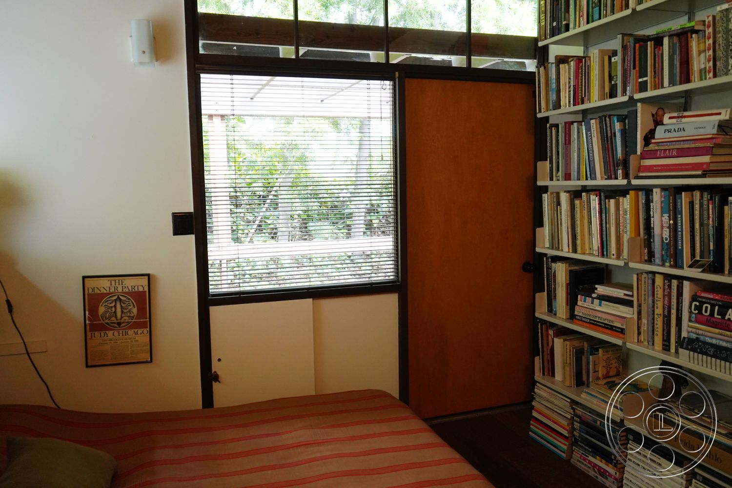 MCM 25 - artwork on wall, hardwood floor, natural light from window, minimalist interior design, greenery view from window, modern residential setting, interior wooden door, exterior wooden door, vertical blinds window treatment, built-in bookshelf with books, striped fabric bedspread, contemporary room layout