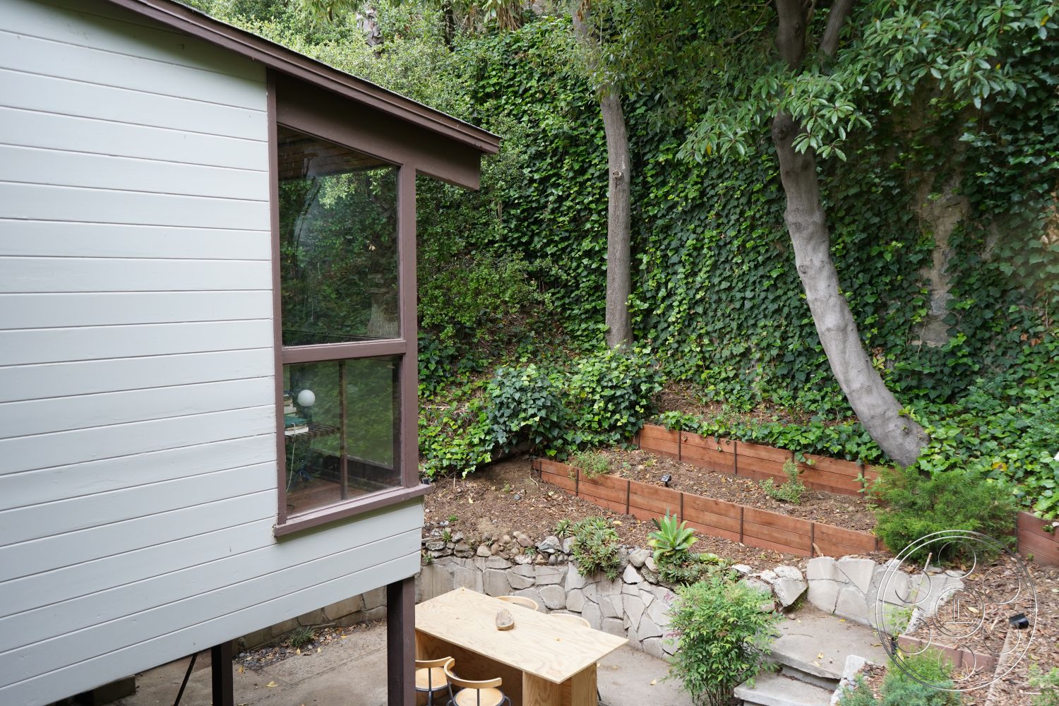 MCM 25 - outdoor dining area, wooden planter boxes, modern architectural style, wood deck patio, stone garden retaining wall, forest setting, exterior wood panel siding, exterior glass window details, natural landscaping with ivy, concrete patio surface, earthy outdoor environment, vegetation accents