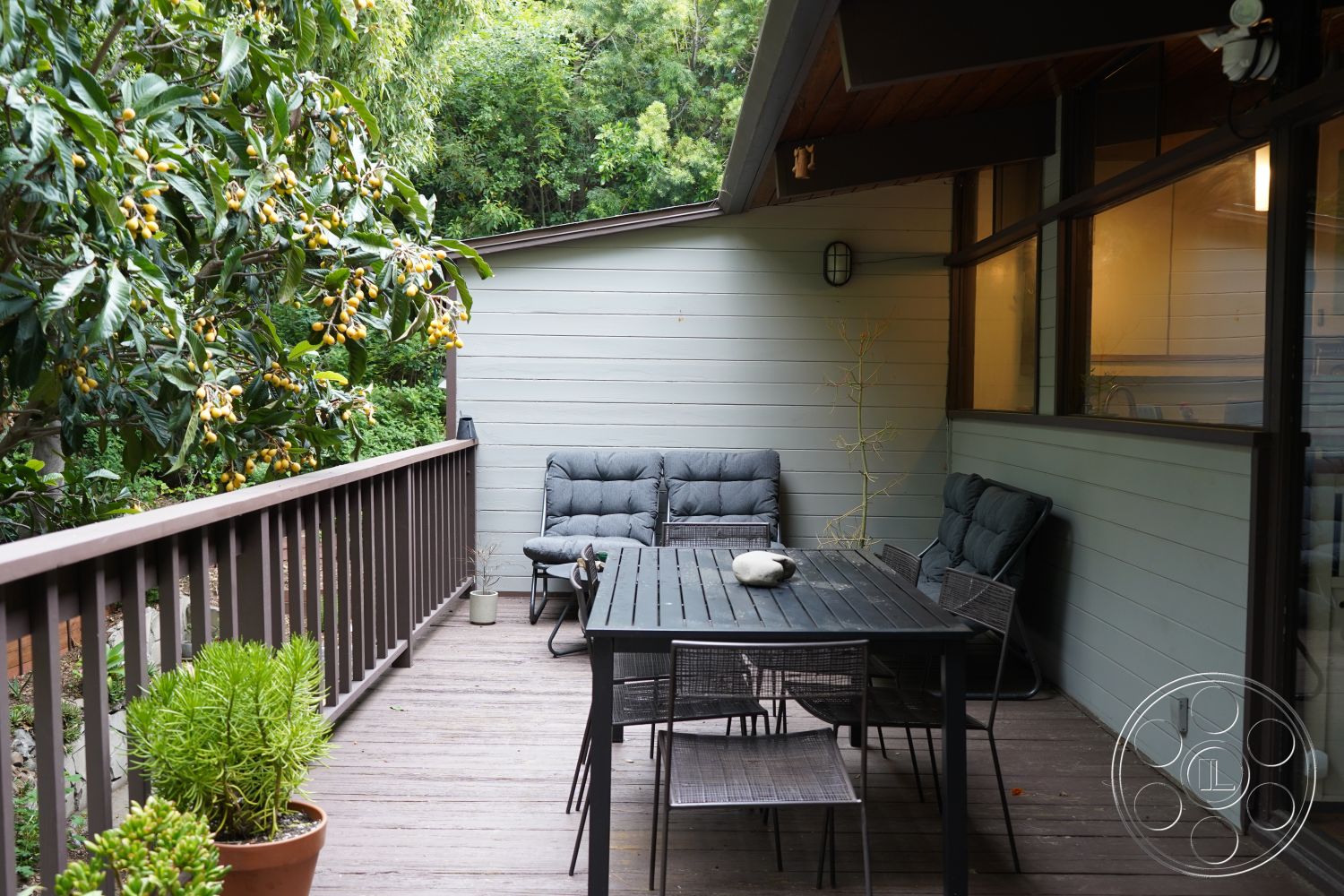 MCM 25 - botanical setting, shaded outdoor seating area, contemporary home design, private garden oasis, wood deck patio flooring, urban garden patio, luxurious outdoor living space, potted succulent plants, open-air relaxation area, exterior klapboard siding walls, metal outdoor dining table, plush outdoor seating cushions, landscaped garden view with greenery, modern outdoor patio area, rustic railing details, insulated sliding glass doors