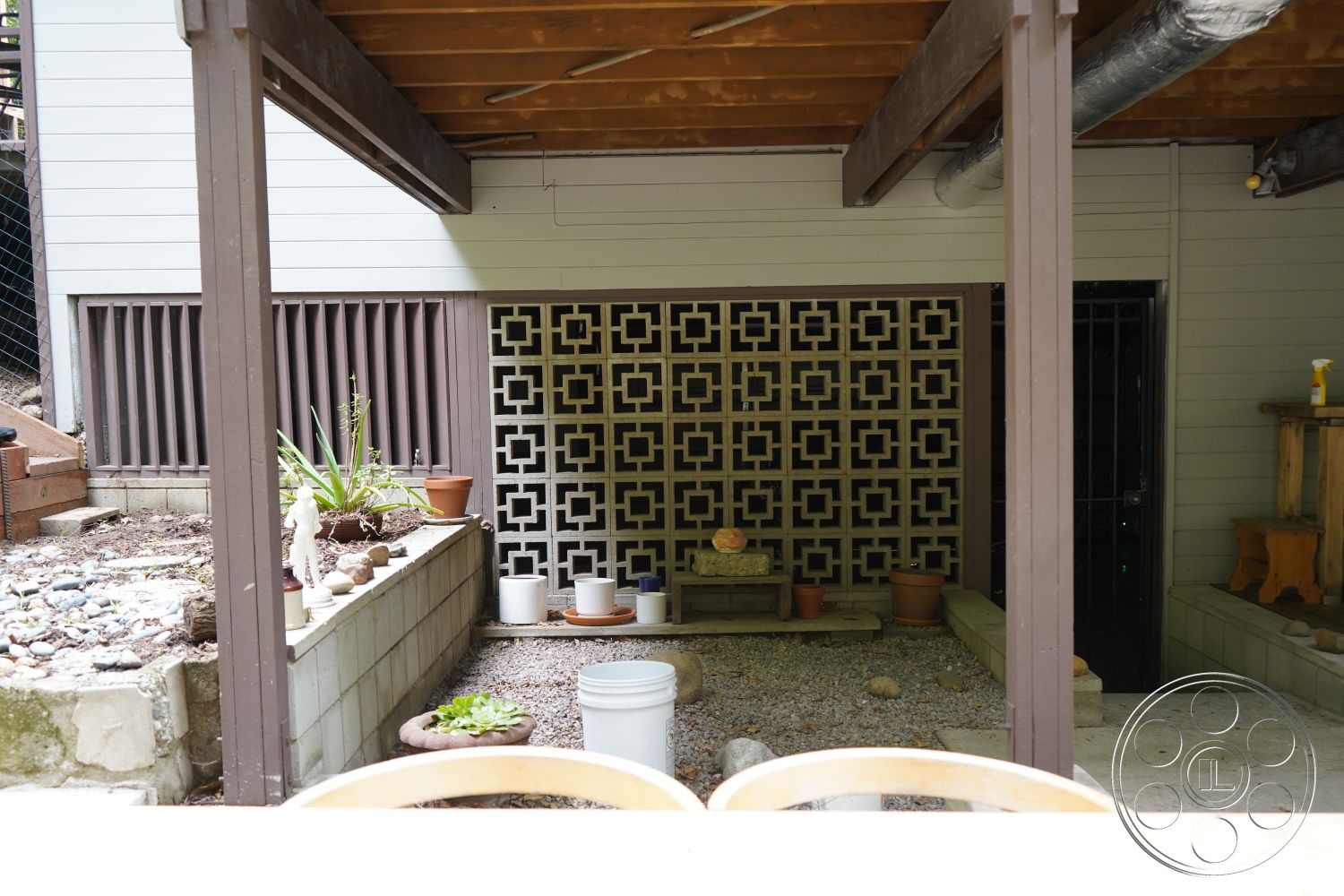MCM 25 - natural stone accents, wooden bench seating, gravel landscaping, modern rustic style, earth-toned color palette, sliding glass door access, textured plaster wall, outdoor garden area, wood beam ceiling, urban backyard setting, exterior patio space, potted plants decor, decorative concrete block wall, open air living space