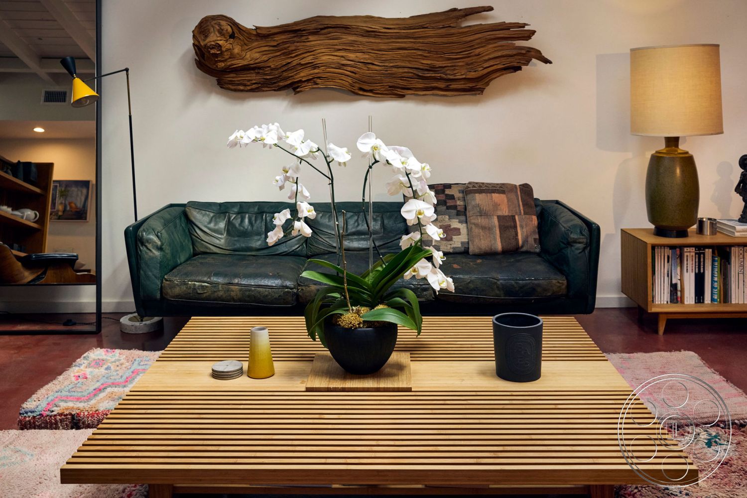 MCM 26 - decorative plant centerpiece, wood accent wall, mid-century modern style, neutral-colored throw pillows, textured wall details, built-in wooden bookshelves, leather sofa in dark green, striped wood coffee table, floor lamp with yellow shade, concrete floor in red, textile area rug with patterns, modern tableware accessories, artistic sculpture decoration, warm lighting from lamp