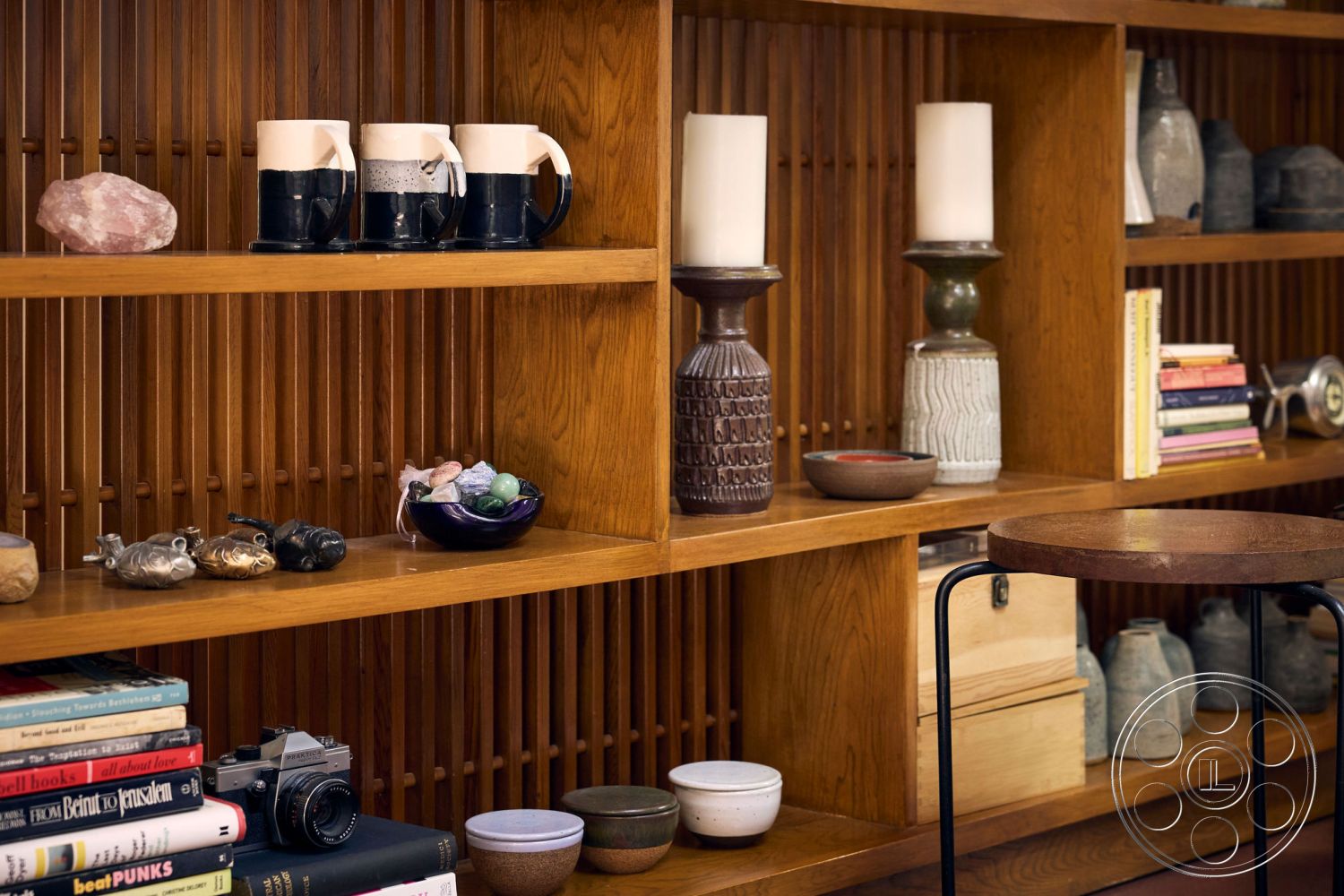 MCM 26 - warm wood tones, mid-century modern furniture, elegant decor elements, modern minimalist design, ceramic decorative vases, glass candle holders, interior wooden shelving units, natural wood accent shelves, stone decorative objects, stacked books on shelves, mix of textures and materials, varied decorative items arrangement, small round side table, reflective surfaces with natural light, colorful ceramic bowls, artistic wooden accents, simple and functional design