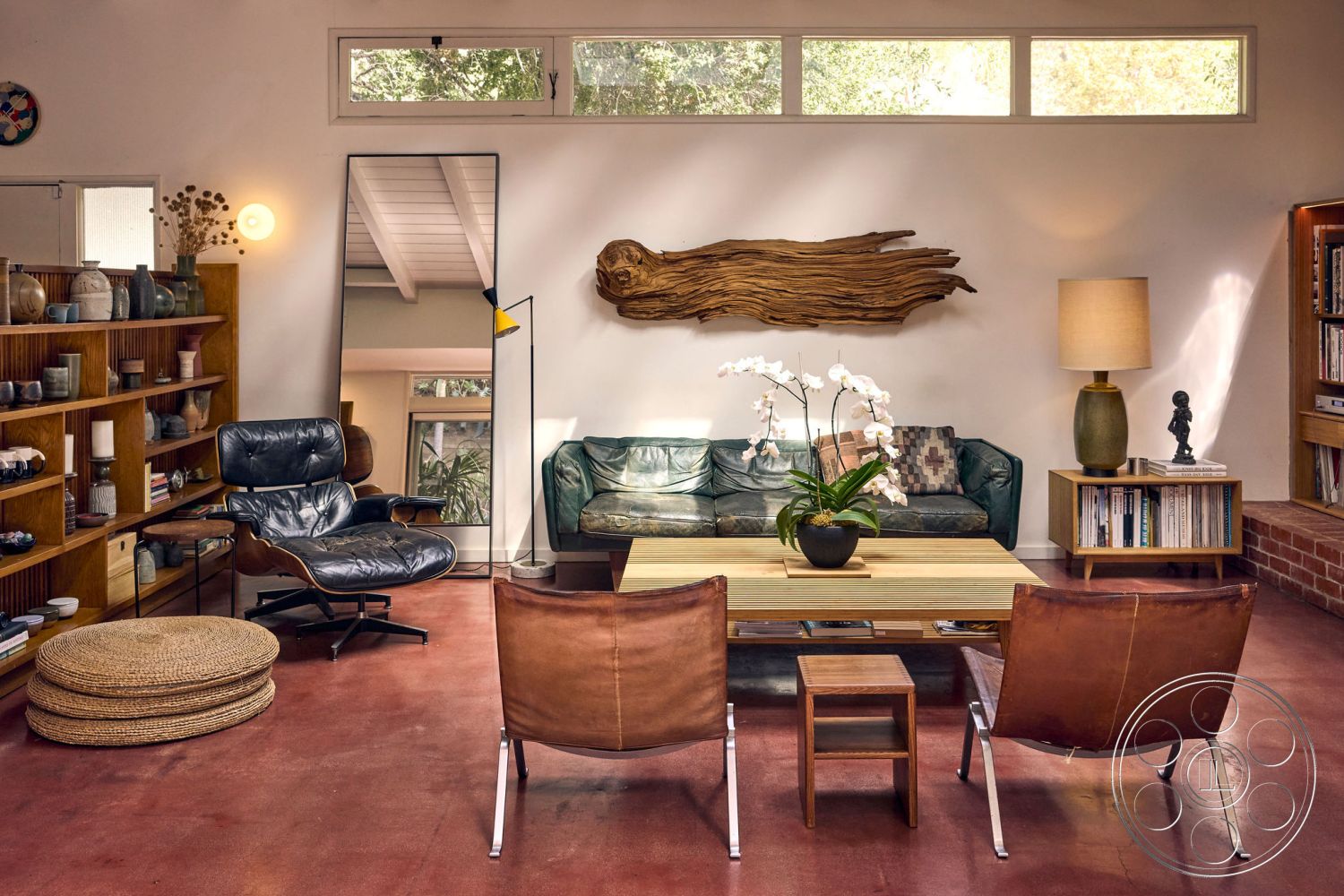 MCM 26 - neutral color palette, polished concrete floor, open floor plan, casual seating area, woven area rug, modern floor lamp, natural wood coffee table, exposed wood ceiling beams, interior living room, large windows with natural light, mid-century modern accent chairs, textured wall paint, green leather sofa, potted orchid centerpiece, sculptural wood wall art, built-in bookshelf with ceramic decor