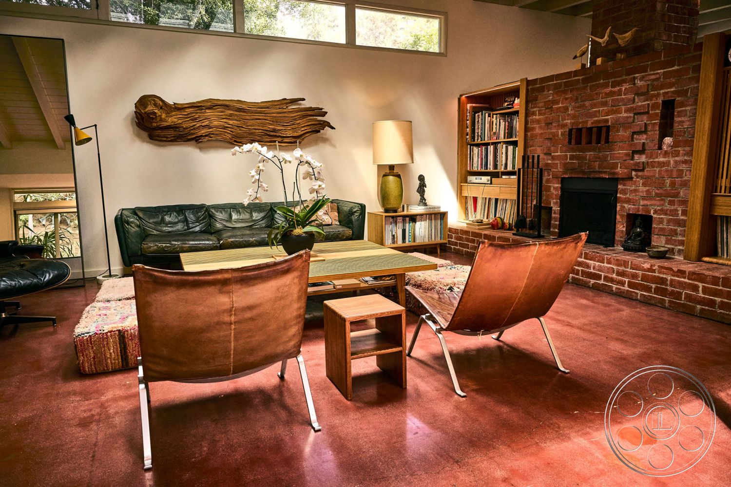 MCM 26 - wooden ceiling beams, soft ambient lighting, open concept living space, textured wall treatments, natural wood accent wall, exposed brick fireplace surround, minimalist interior design, interior concrete flooring, large windows providing natural light, dark leather sofa, mid-century modern coffee table, metal chair frame with leather seating, built-in bookshelf with wooden cabinetry, patterned woven area rug, curated home decor accents, sculptural houseplant arrangement, artistic wall sculpture, cozy conversational seating arrangement