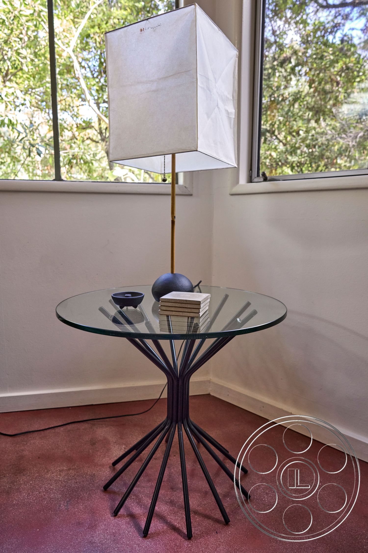 MCM 26 - interior minimalist decor, interior glass tabletop, interior black metal base table, interior modern side table, interior natural light setting, interior white paper lampshade, interior artistic stone decorative, interior wooden coasters stack, interior sleek surface finish, interior contemporary furnishings, interior hardwood floor option, interior neutral color scheme, interior glass and metal combination