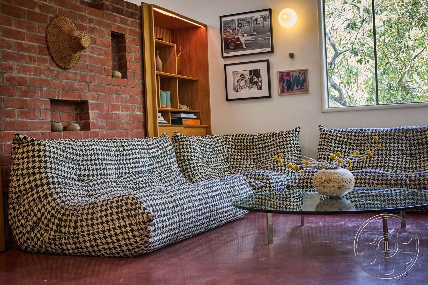 MCM 26 - polished concrete flooring, textured plaster walls, contemporary coffee table, natural light filling the space, minimalist interior design, exposed brick accent wall, glass tabletop with metal legs, hounds-tooth patterned upholstered seating, open wall shelves for décor, vaulted interior ceiling, nature view through large window, artistic wall décor with photographs, casual living room arrangement, modern home office nook, functional use of space