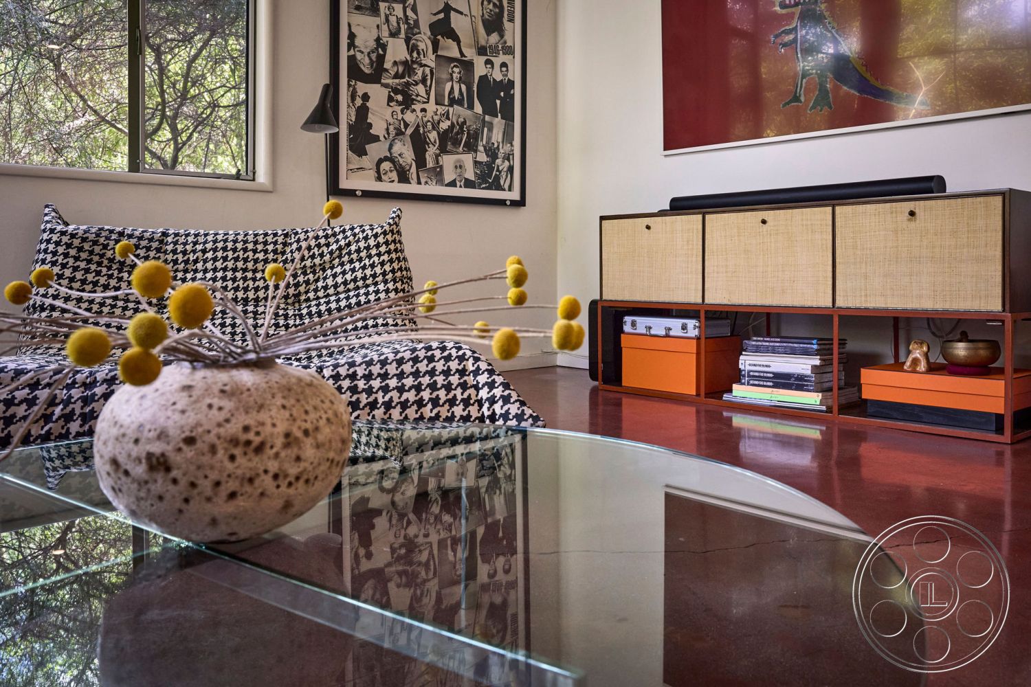 MCM 26 - minimalist decor, glass coffee table, natural light from large windows, colorful decorative accents, modernist architecture, mid-century modern design, exposed wood ceiling beams, interior concrete floors, black and white houndstooth sofa, woven rattan storage unit, artistic wall prints, rounded vase with floral arrangement