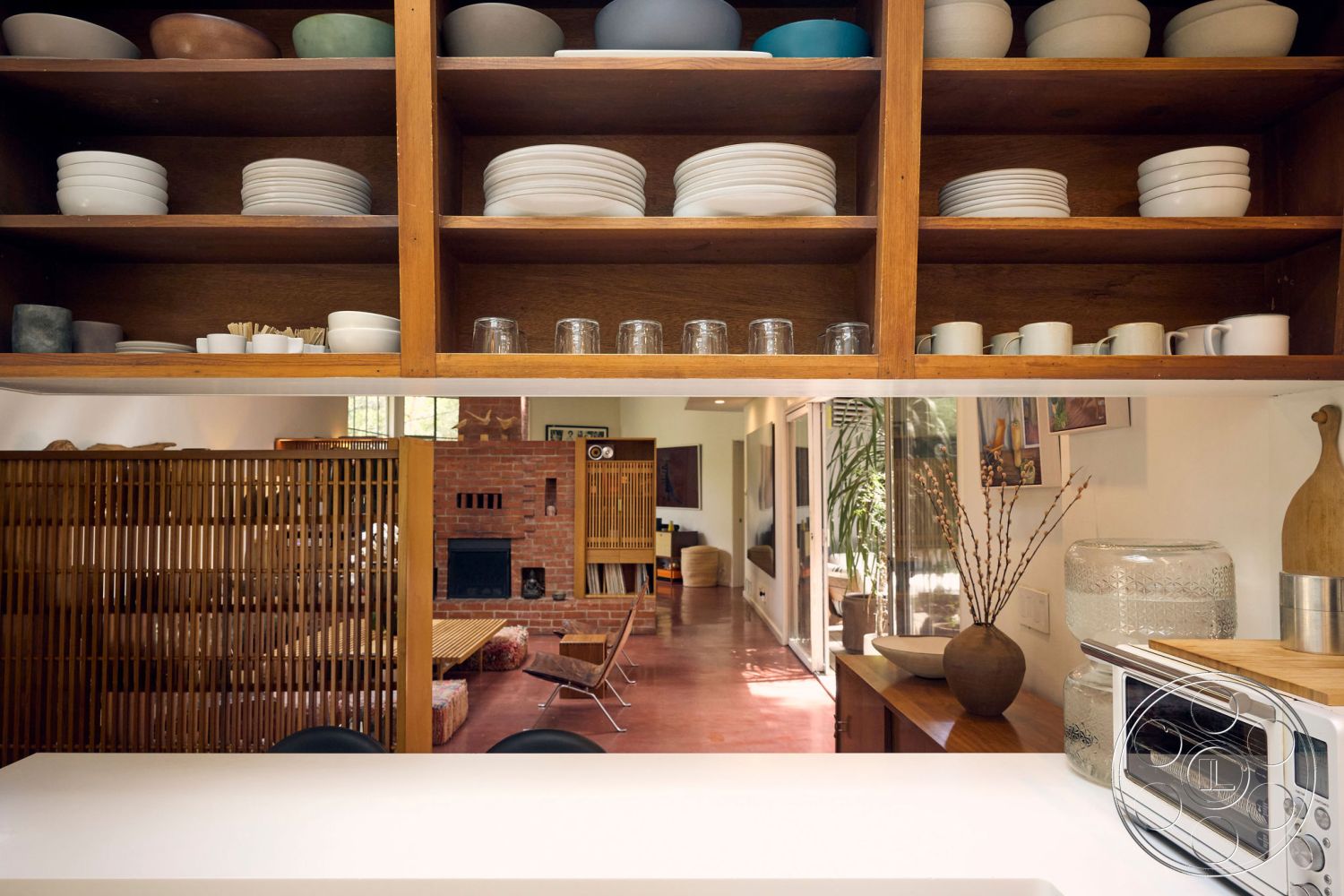 MCM 26 - interior, wood cabinetry, open shelving units, terracotta tile flooring, built-in kitchen shelves, interior, red brick fireplace wall, modern living room, minimalist design, natural light ambiance, interior, white quartz countertop, bar seating, contemporary kitchen, clear glass storage jars, decorative vases, interior, bamboo room divider, acoustic treatment details, mid-century modern furnishings, interior, polished plaster walls, neutral color palette, modern art decor, house plants, interior, exposed wood ceiling beams, vaulted ceilings, light-filled spaces, open-concept layout, interior, minimalist dining area, round wooden dining table, absence of clutter, cozy atmosphere, interior, contemporary sofa, area rugs, floor-to-ceiling windows, serene indoor environment