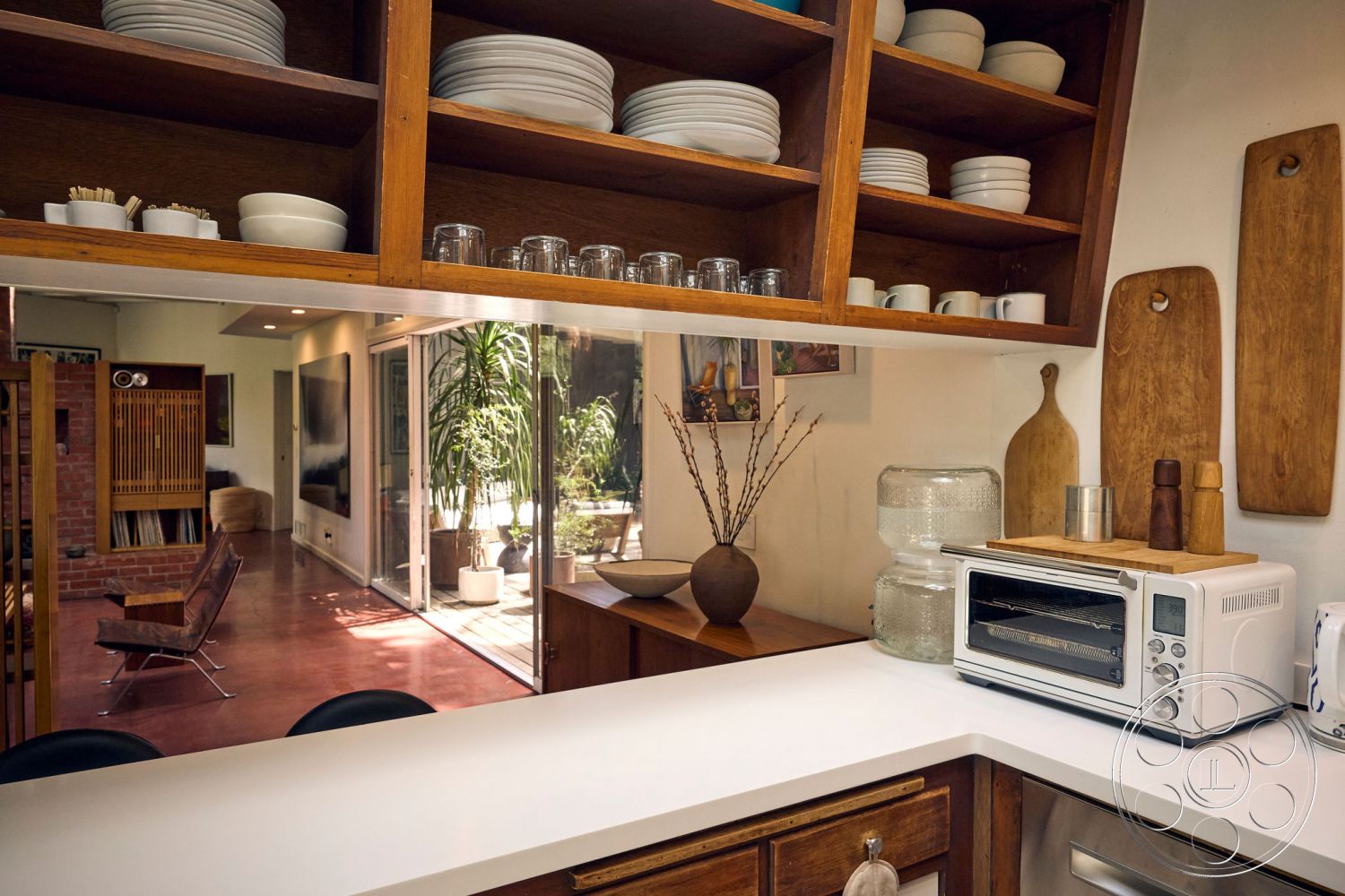 MCM 26 - glass sliding doors interior, neutral color palette interior, exposed brick accent wall interior, open shelving kitchen, polished concrete flooring interior, mid-century modern design interior, hardwood kitchen cabinets interior, white quartz countertop kitchen, stainless steel appliances kitchen, wooden cutting boards kitchen, decorative vase with branches interior, modern bar stools interior, natural light from patio interior, minimalist kitchen design interior, integrated lighting fixtures interior, plant accent interior, multi-purpose living space interior