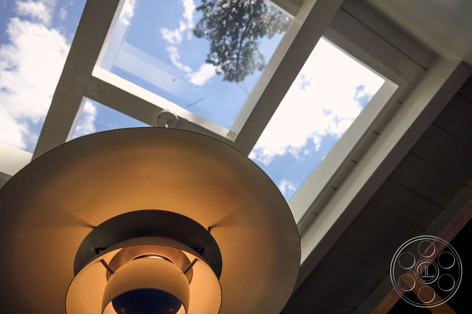 MCM 26 - minimalist design, wooden ceiling beams, circular pendant light, modern lighting fixture, skylight ceiling, white painted ceiling, exposed wooden support structure, natural light indoors, cloudy sky view, bright indoor atmosphere