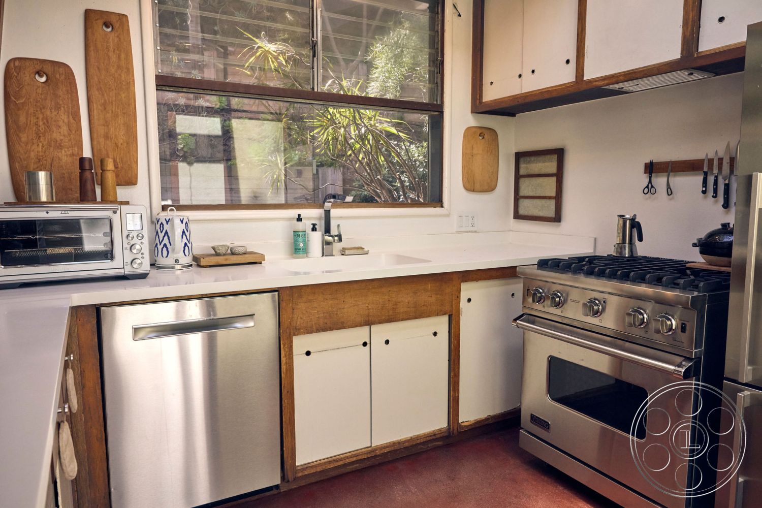 MCM 26 - stainless steel appliances, functional kitchen layout, warm wood accents, interior kitchen design, minimalist kitchen design, white quartz countertops, bright interior lighting, tile kitchen backsplash, wood cabinetry with natural finish, contemporary sink with modern faucet, open shelving with cutting boards, kitchen window with greenery view, modern gas range stove, chrome dishwasher, exposed decorative kitchen elements, cooking area with organization tools