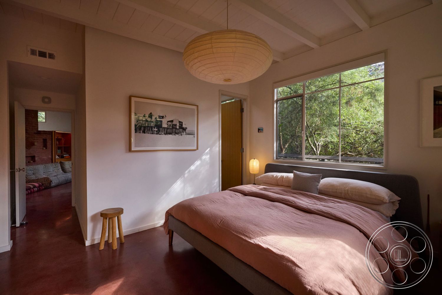 MCM 26 - neutral color palette, natural light, minimalist design, open floor plan, concrete flooring, modern pendant lighting, artwork on walls, cozy ambiance, contemporary aesthetic, round side table, wood accent furniture, interior bedroom, wood beam ceiling, large windows with greenery view, textured bed linens, sliding door entry, paper lantern light fixture