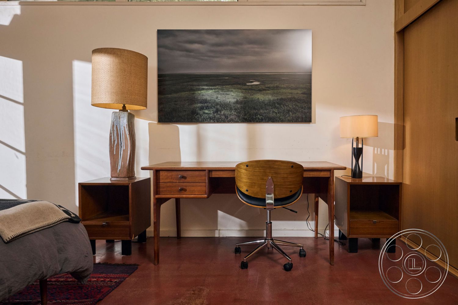 MCM 26 - open space layout, warm color palette, functional workspace, artwork on wall, textured wall treatment, natural light from window, simple geometric shapes, minimalist room design, interior hardwood flooring, exposed brick accent wall, contemporary floor lamp, contemporary table lamp, mid-century modern desk, metal rolling chair, wooden nightstand with drawer, polished concrete wall, retro style decor, natural materials accent, inviting and cozy atmosphere