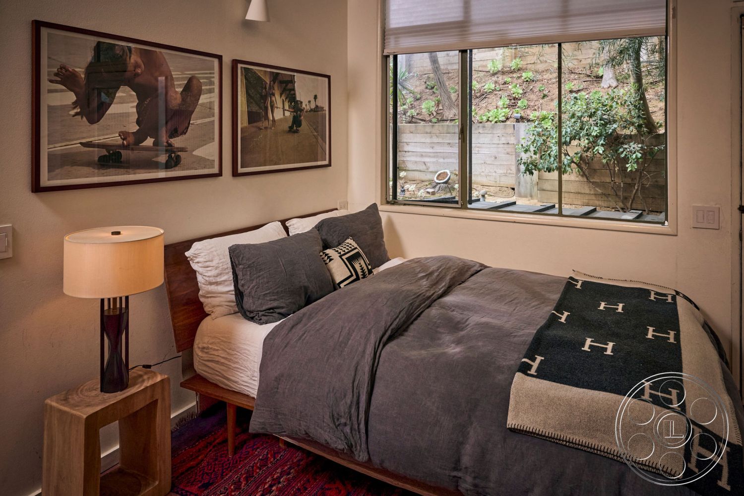 MCM 26 - minimalist decor, wooden bedside table, greenery view, modern aesthetic, concrete walls, floor-to-ceiling windows, framed wall art, area rug with geometric patterns, wooden window frame, interior bedroom, textured plaster wall, natural light-filled space, lampshade table lamp, hardwood bed frame, neutral bedding, comfortable sleep space