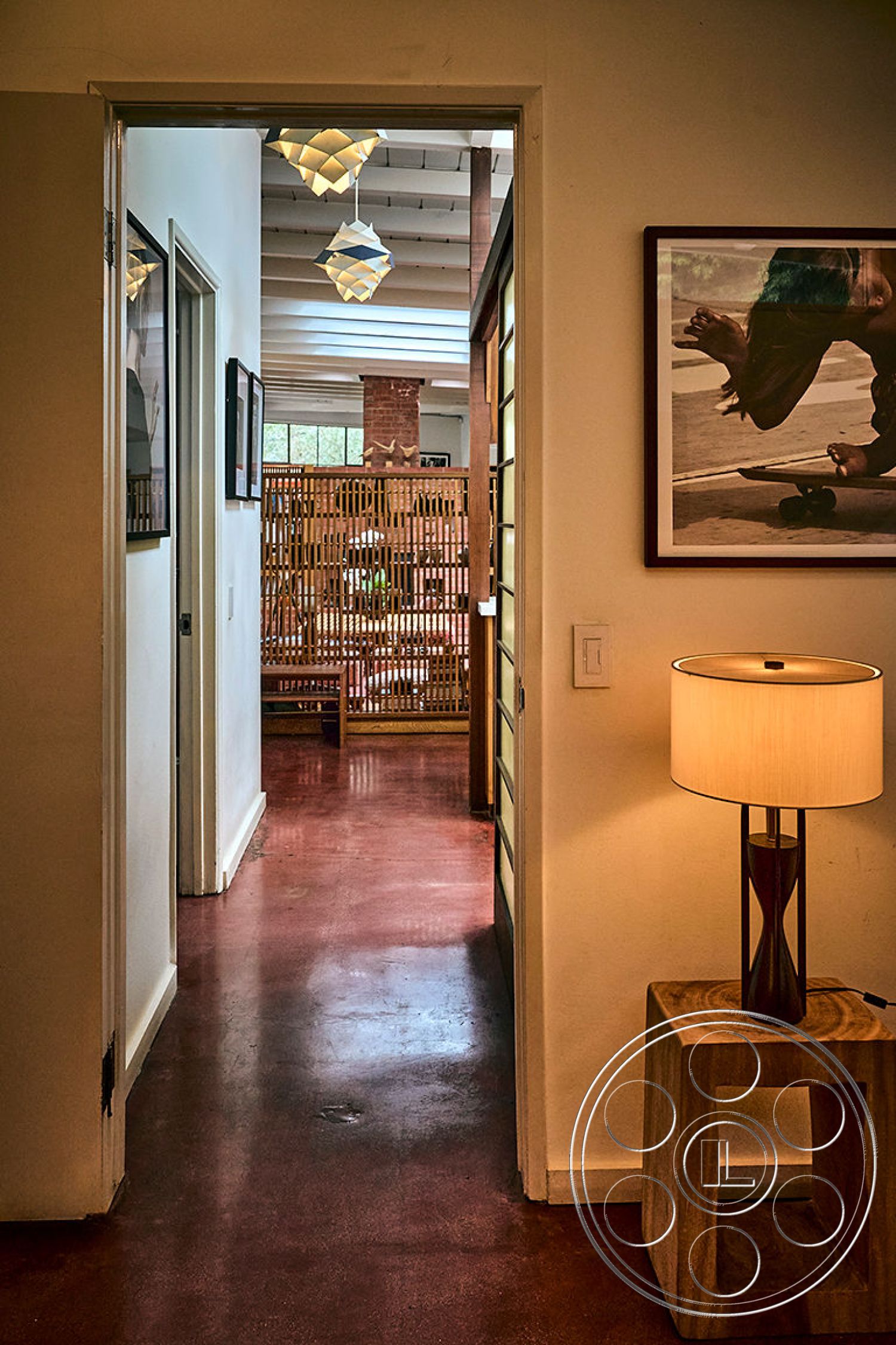 MCM 26 - minimalist decor, modern pendant lighting, warm color palette, modern aesthetic, natural light from large windows, textured wall treatments, wooden accent table, exposed wood ceiling beams, neutral painted walls, concrete floor with a polished finish, bamboo room divider, open floor plan hallway, artwork framed on the wall, architectural details with clean lines, comfortably furnished living space