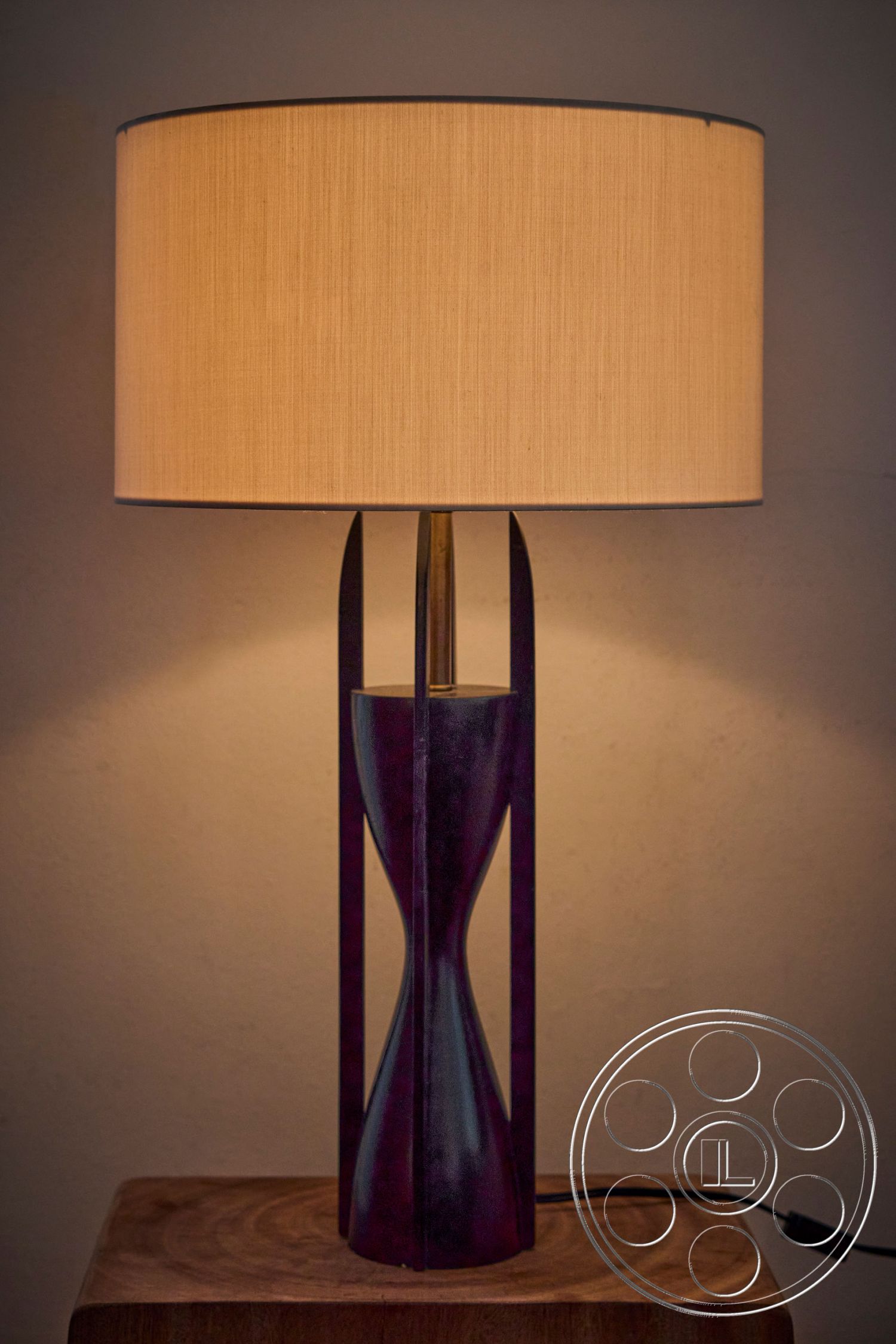 MCM 26 - gold accents, wooden side table, decorative table lamp, contemporary home decor, interior lighting fixture, fabric lampshade, ambient light source, metal lamp base, modern lamp design, symmetrical lamp shape, ellipse-shaped lamp base, stylish bedside lamp, minimalist style lighting, elegant lighting solution, purple-toned lamp base, soft lighting effect, crafted home accessory