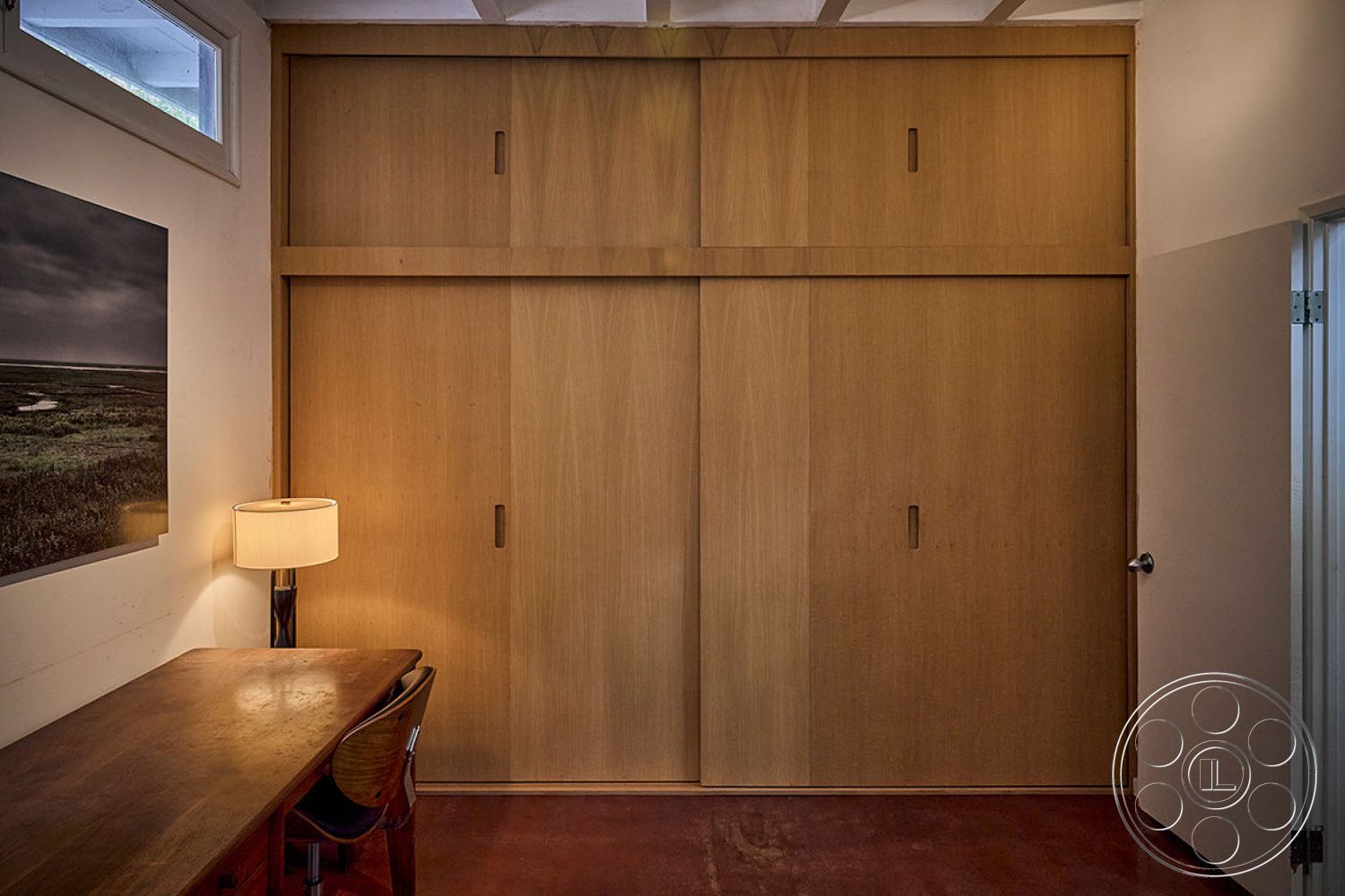 MCM 26 - minimalist design, contemporary artwork, warm color palette, smooth concrete flooring, dark wood desk, modern table lamp, open-beam ceiling, interior wood paneling walls, sliding wooden closet doors