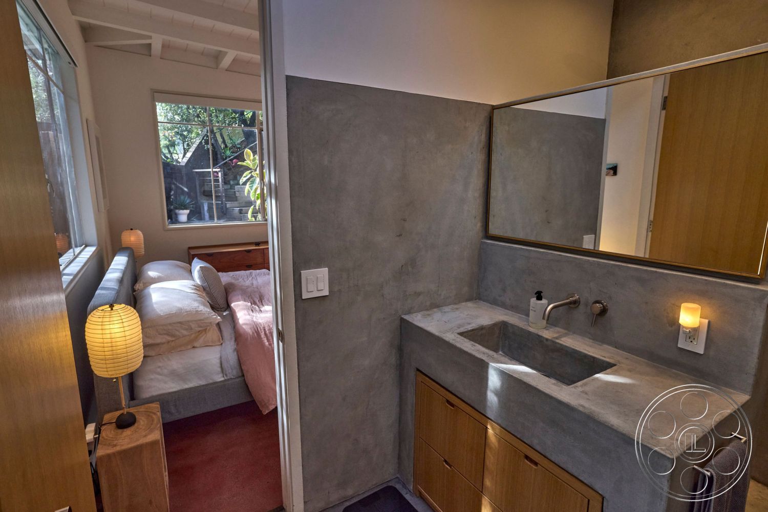 MCM 26 - neutral color palette, open concept layout, contemporary interior style, interior bathroom space, large window with garden view, concrete countertop vanity, textured plaster accent wall, flush-mounted ceiling lights, suburban garden setting, warm lighting fixtures, exposed concrete bathroom walls, wooden cabinetry with minimalist design, light hardwood bedroom flooring, modern rectangular mirror