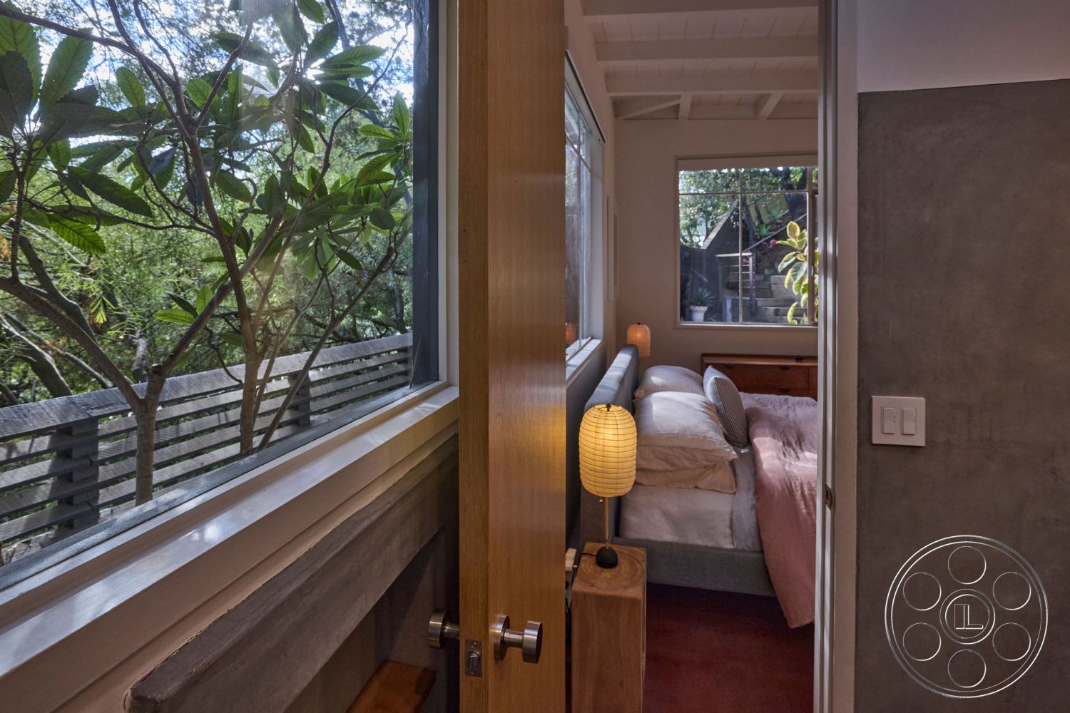 MCM 26 - exposed beam ceiling, modern pendant lighting, minimalist furniture, floor-to-ceiling windows, contemporary design elements, textured plaster wall, natural light-filled space, wooden door frame, serene forest setting, concrete wall interior, hardwood bedroom floor, bedroom area with soft textiles, landscape view through window