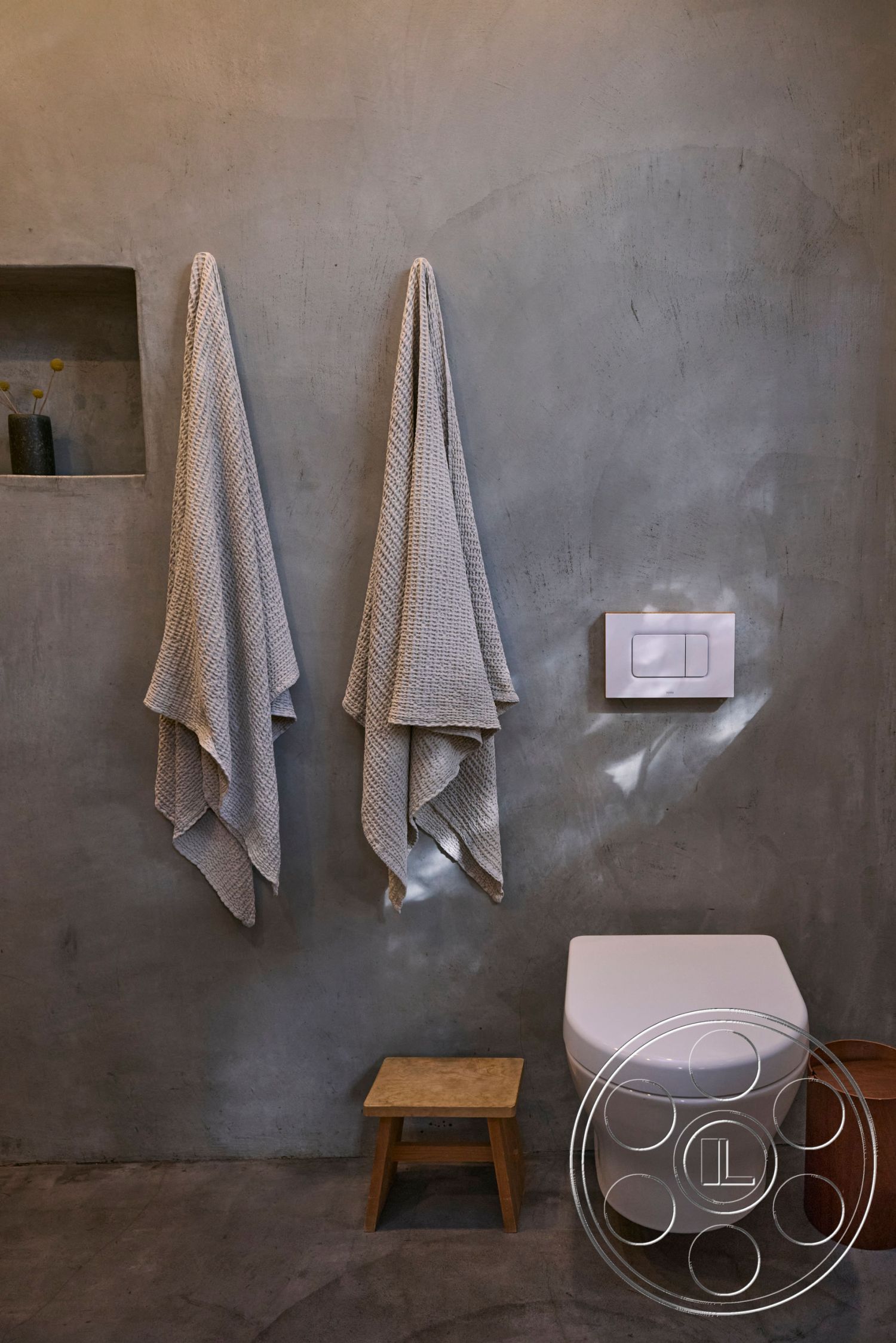 MCM 26 - neutral color palette, spa-like atmosphere, polished concrete flooring, subtle ambient lighting, interior bathroom, exposed concrete bathroom walls, minimalist toilet design, wooden stool seating, textured cotton towels, modern flush toilet, contemporary bathroom accessories, open wall niche for decor, urban minimalist restroom, functional yet stylish design