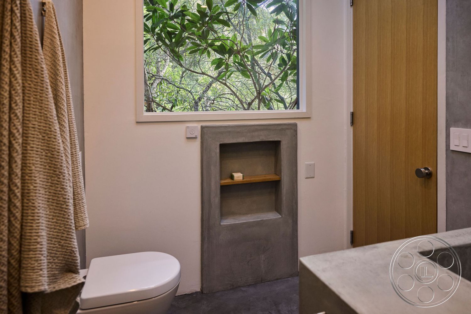 MCM 26 - natural light, minimalist design elements, textured plaster walls, neutral color scheme, wood door, interior bathroom, concrete bathroom flooring, modern toilet design, concrete shower niche, concrete bathroom walls, large window with greenery view, exposed wood shelf