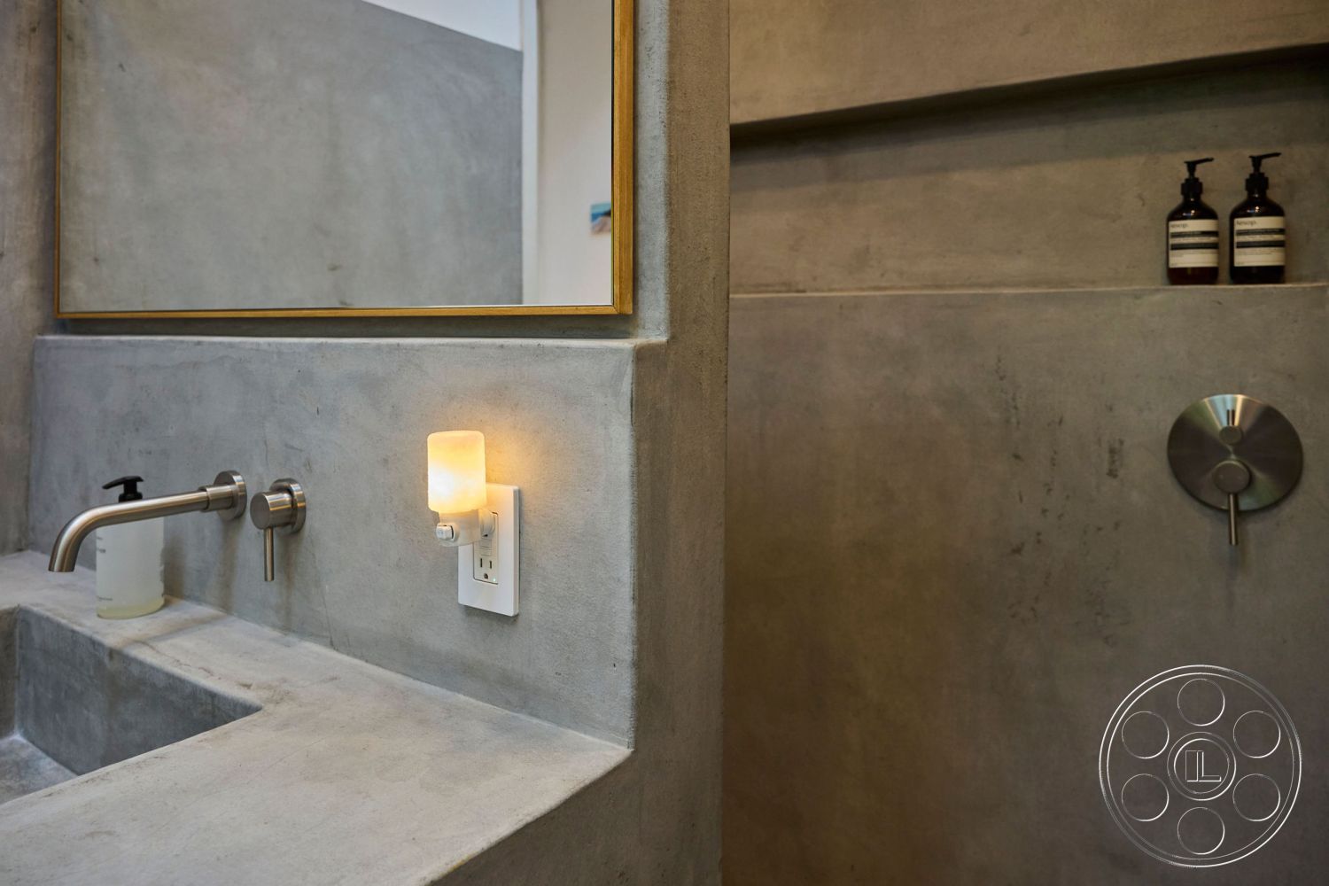 MCM 26 - minimalist bathroom design, textured plaster wall finish, concrete sink countertop, stainless steel faucet, exposed concrete wall interior, modern wall-mounted light fixture, floating concrete shelf, bronze-framed mirror, sealed concrete surface, linear wall-mounted shower control