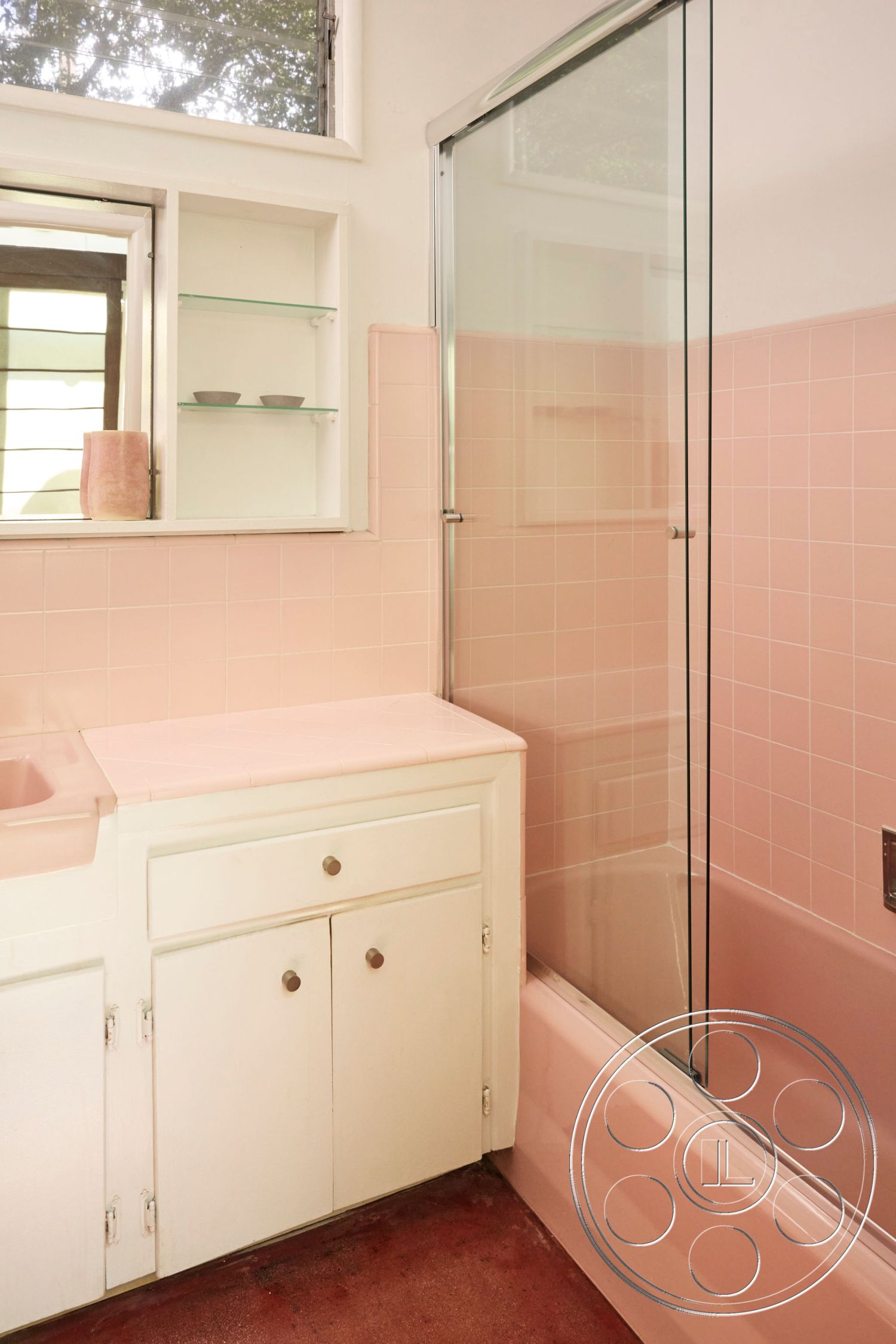 MCM 26 - minimalist aesthetic, simple contemporary design, glass shower doors, interior bathroom, red concrete flooring, pink tile shower wall, pink tile bathtub, white laminate bathroom vanity, silver cabinet hardware, open shelving above vanity, horizontal window for natural light