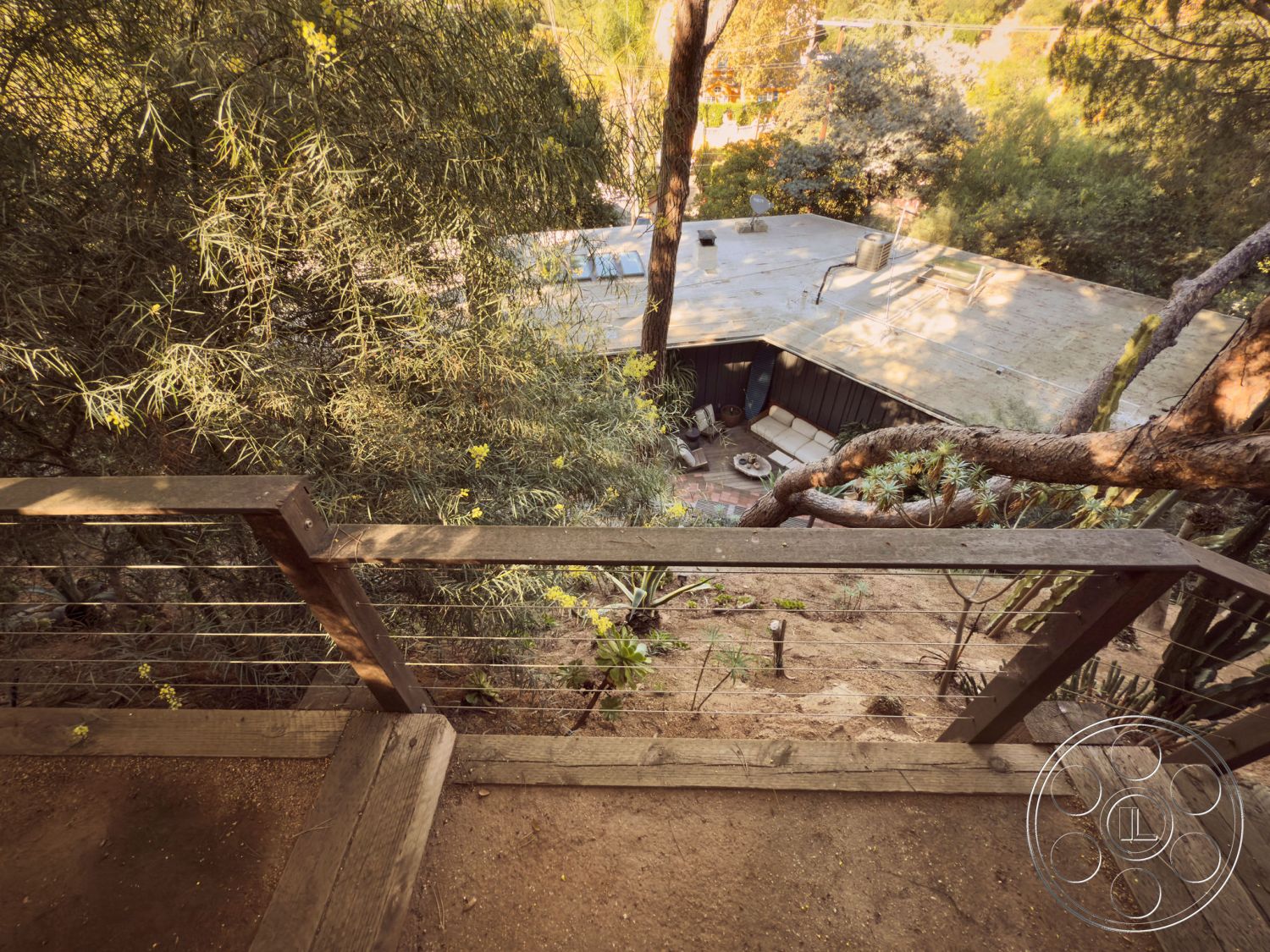 MCM 26 - outdoor living space, surrounding forest setting, modern outdoor seating area, surrounding trees and greenery, exterior wooden deck railing, exposed wood deck steps, paved stone firepit area, natural landscaping with native plants, rustic hillside home view, circular patio layout, gentle slope yard, contemporary home architecture, wooden balcony perspective, open-air outdoor design, cactus and succulent plants