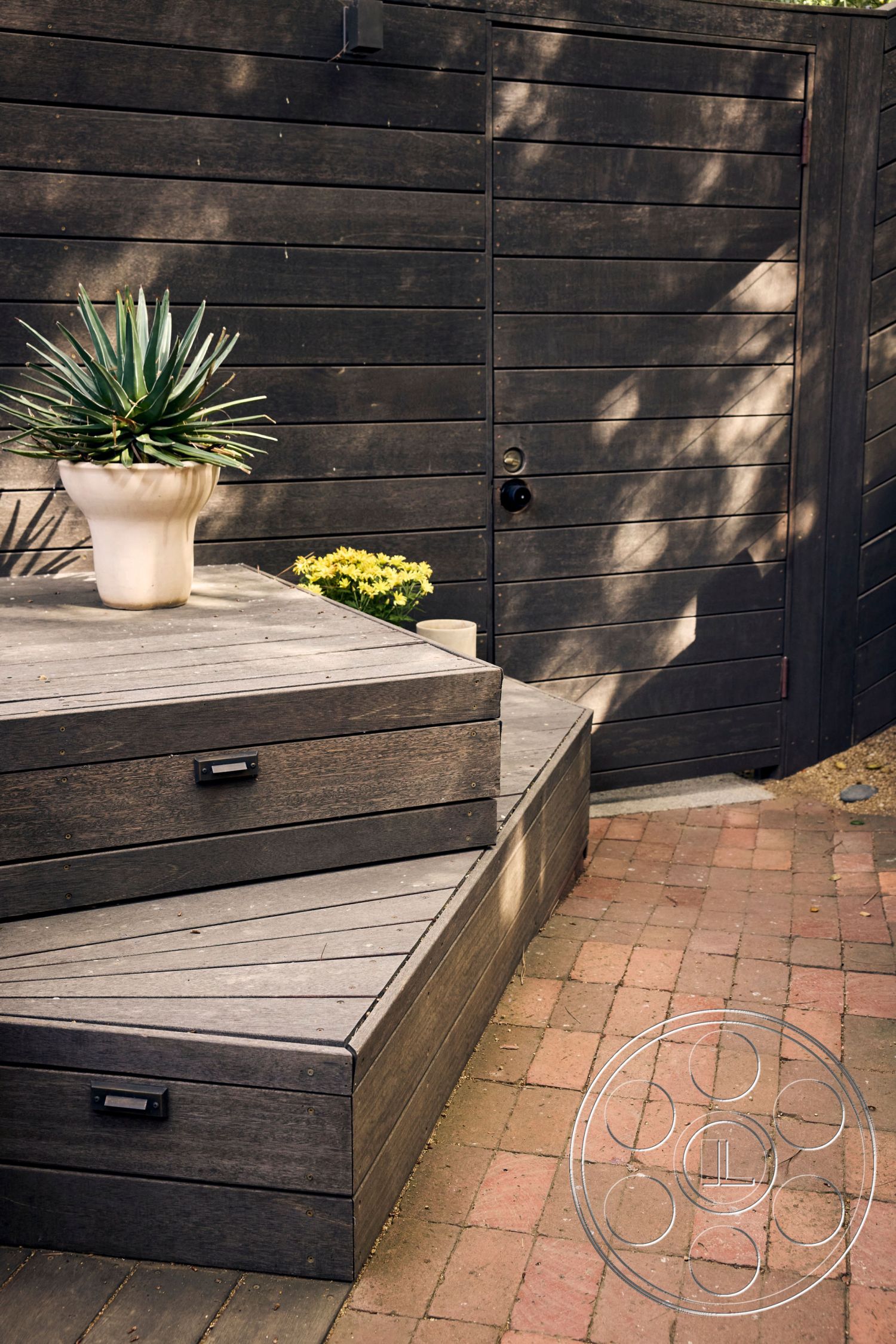 MCM 26 - landscaped garden area, exterior wood deck steps, minimalist outdoor design, dark-stained wood terrace, patio with brick pavers, plant container with succulents, textured wooden fence, modern outdoor entrance, rectangular garden steps, elevated wooden seating